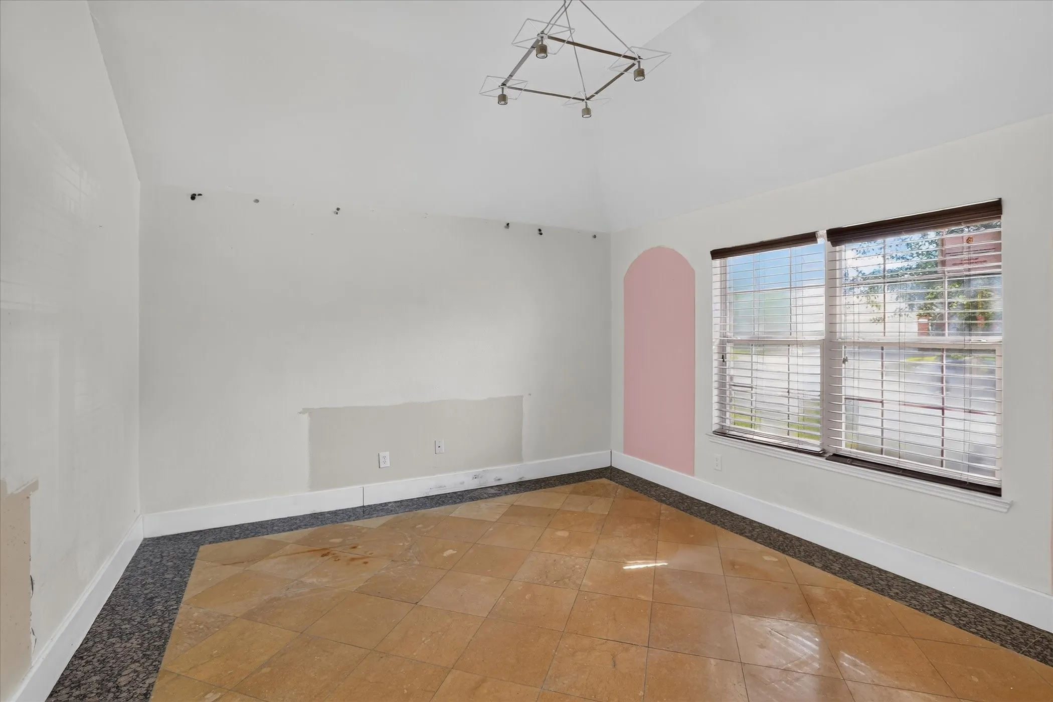 Vaulted ceiling with an attached light fixture, a large window with blinds, and tiled flooring with a dark border