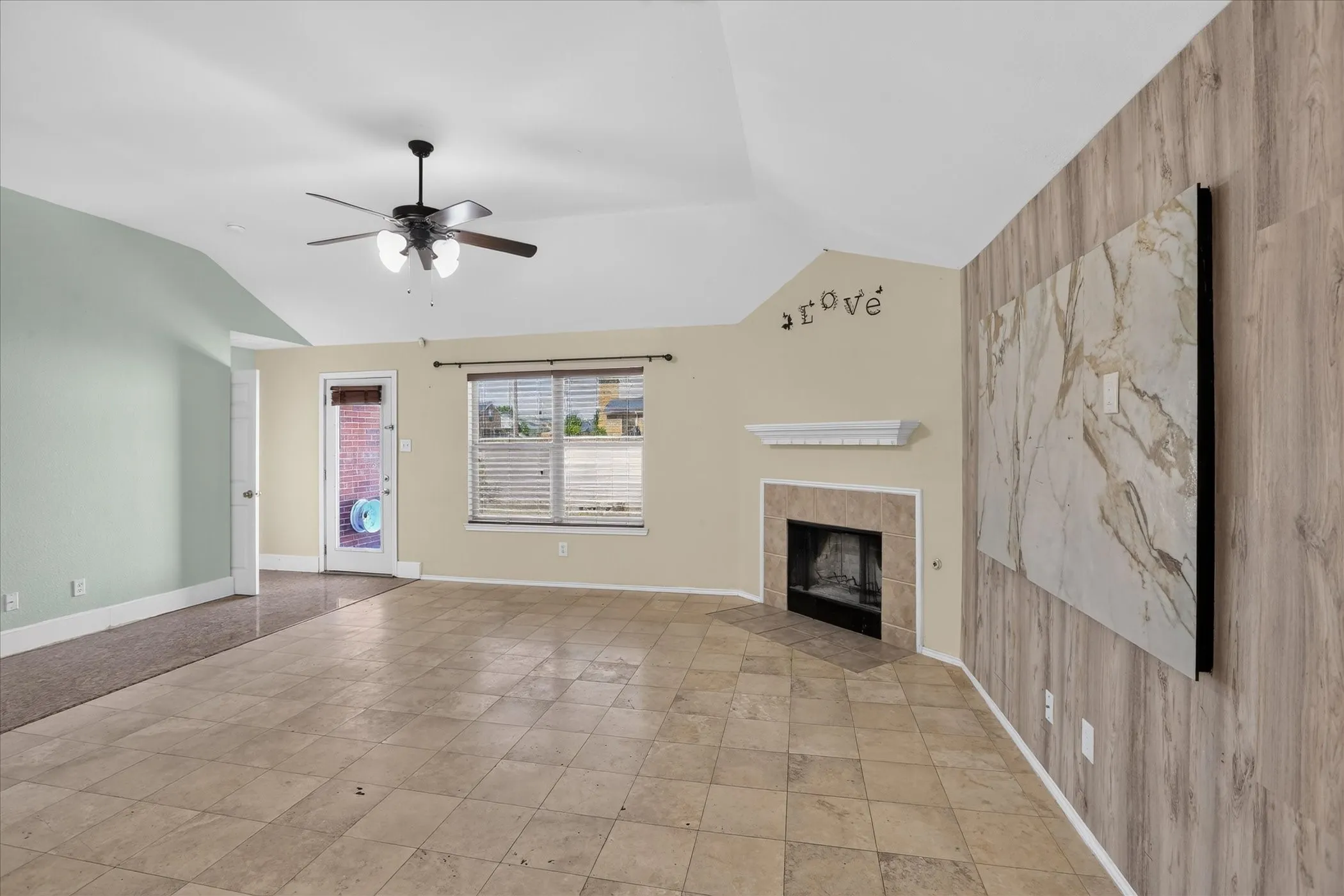 Vaulted ceiling with a ceiling fan, tile flooring, fireplace with mantel, and wood-look accent wall