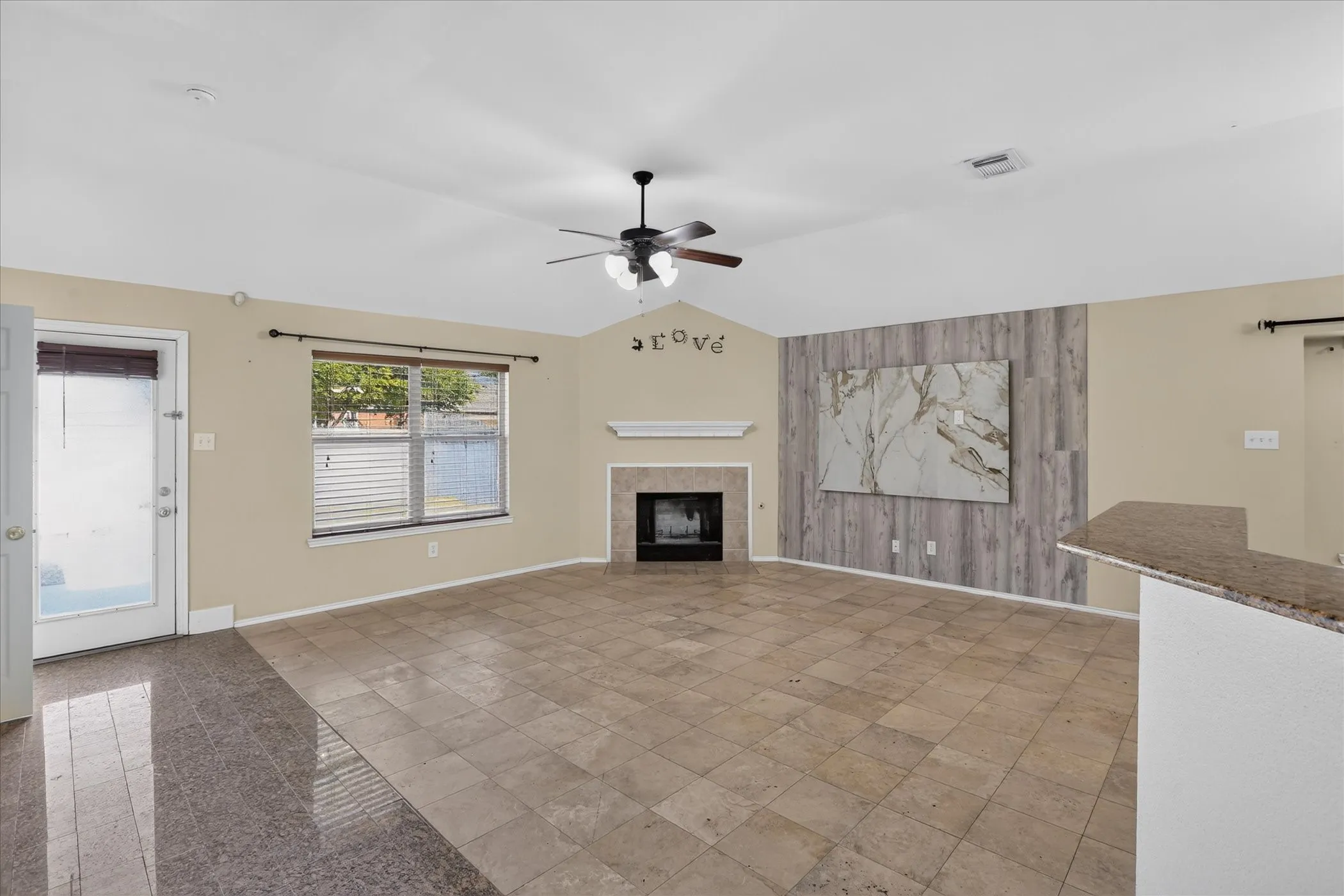 Vaulted ceiling with a ceiling fan, tiled flooring, built-in fireplace with mantel, accent wall with wood-finish paneling, and a bar-height countertop