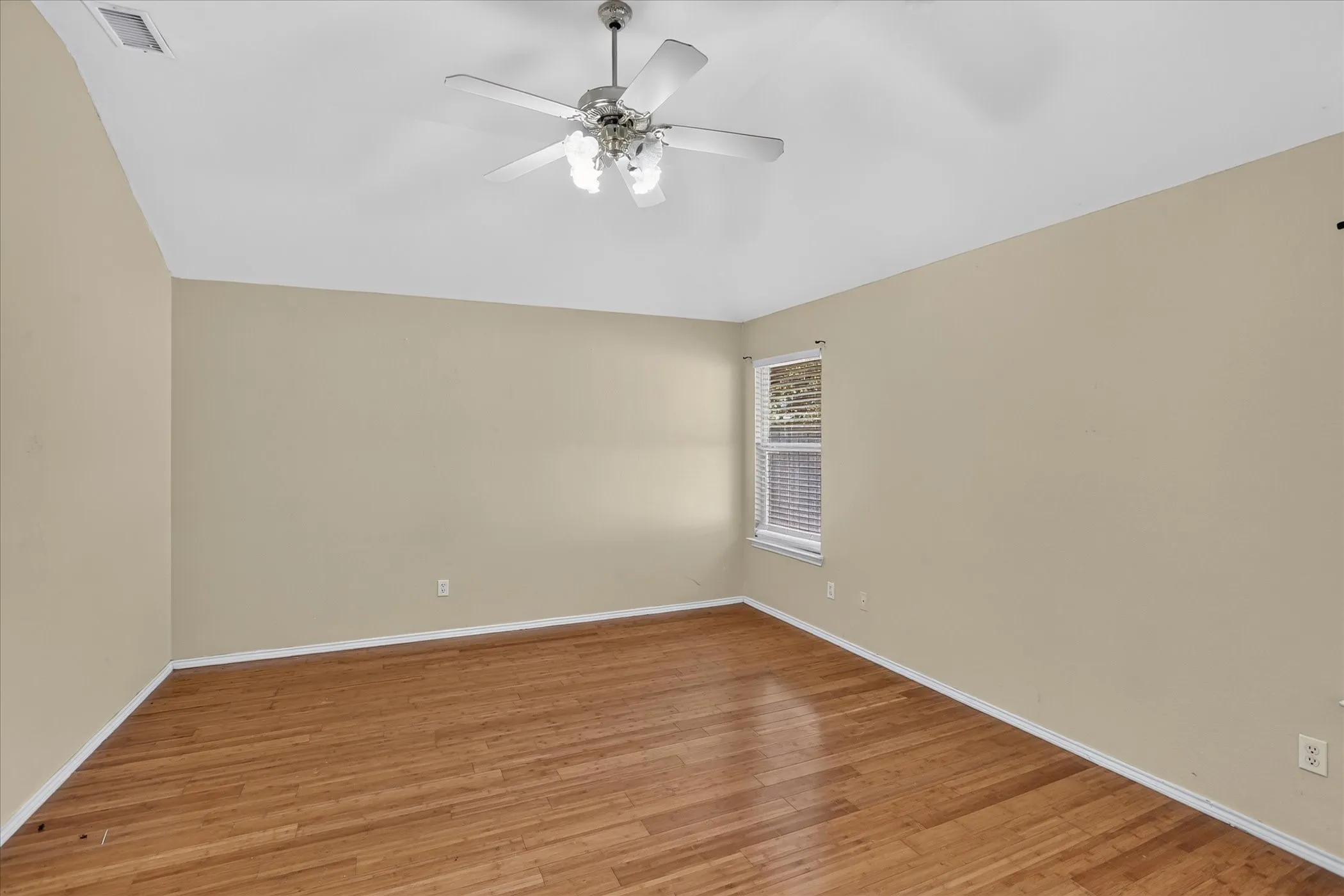 Wood-finish flooring, neutral wall tones, window with horizontal blinds, and a ceiling fan with integrated lighting