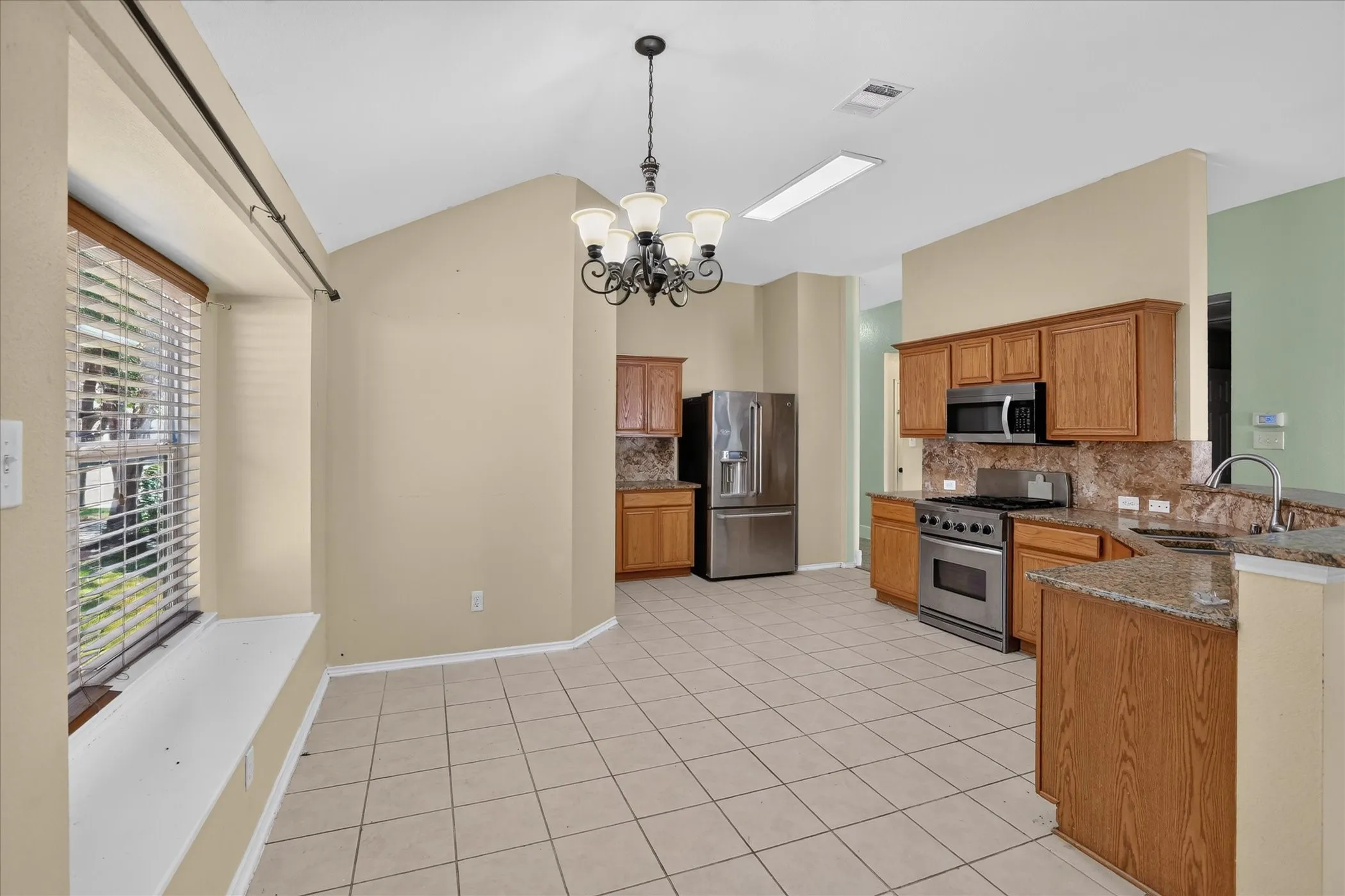 Spacious kitchen featuring stainless steel appliances, wood cabinetry, granite-finish countertops, and a tile backsplash