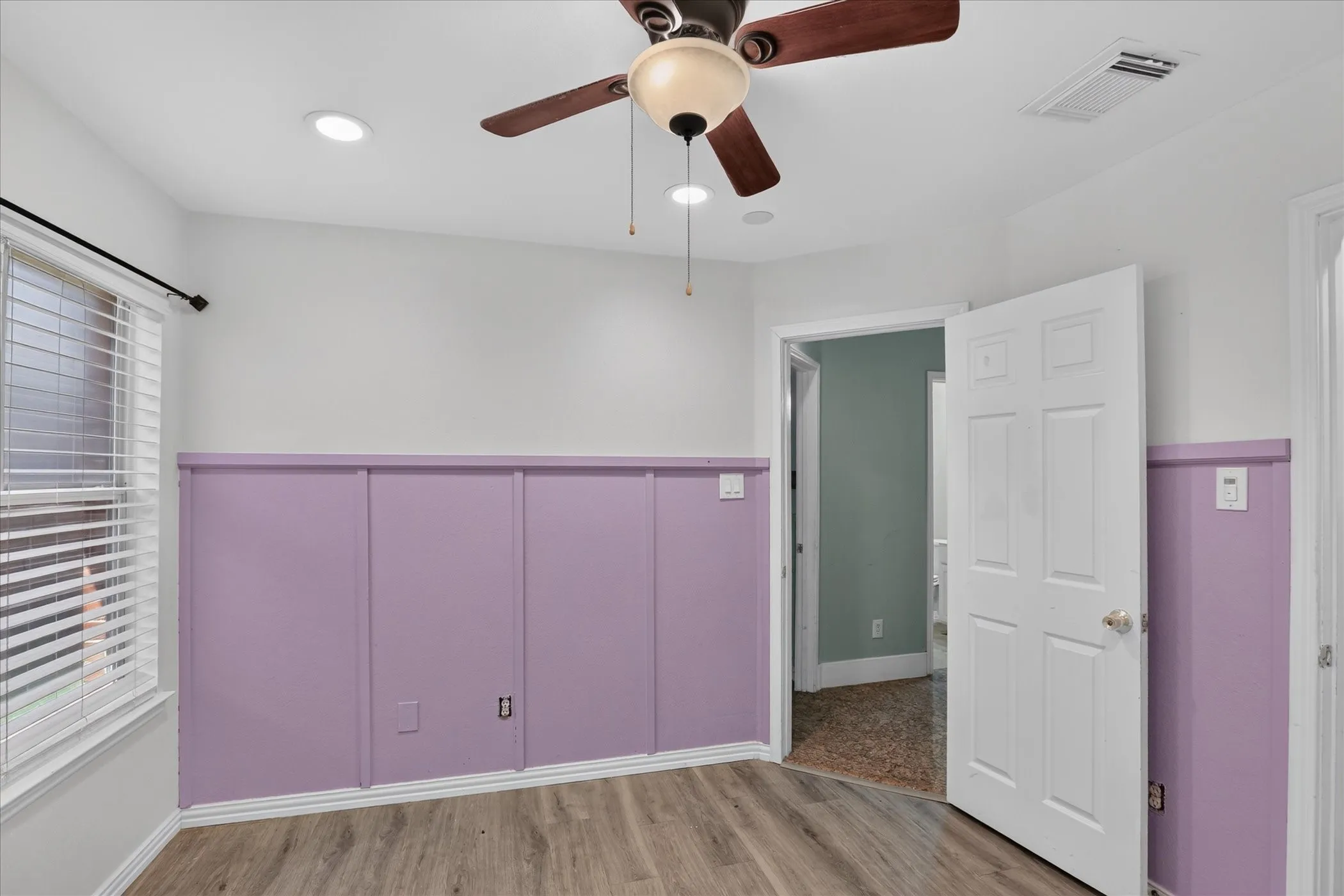 Wood-finish flooring, recessed lighting, ceiling fan, window with blinds, and paneled wall detailing