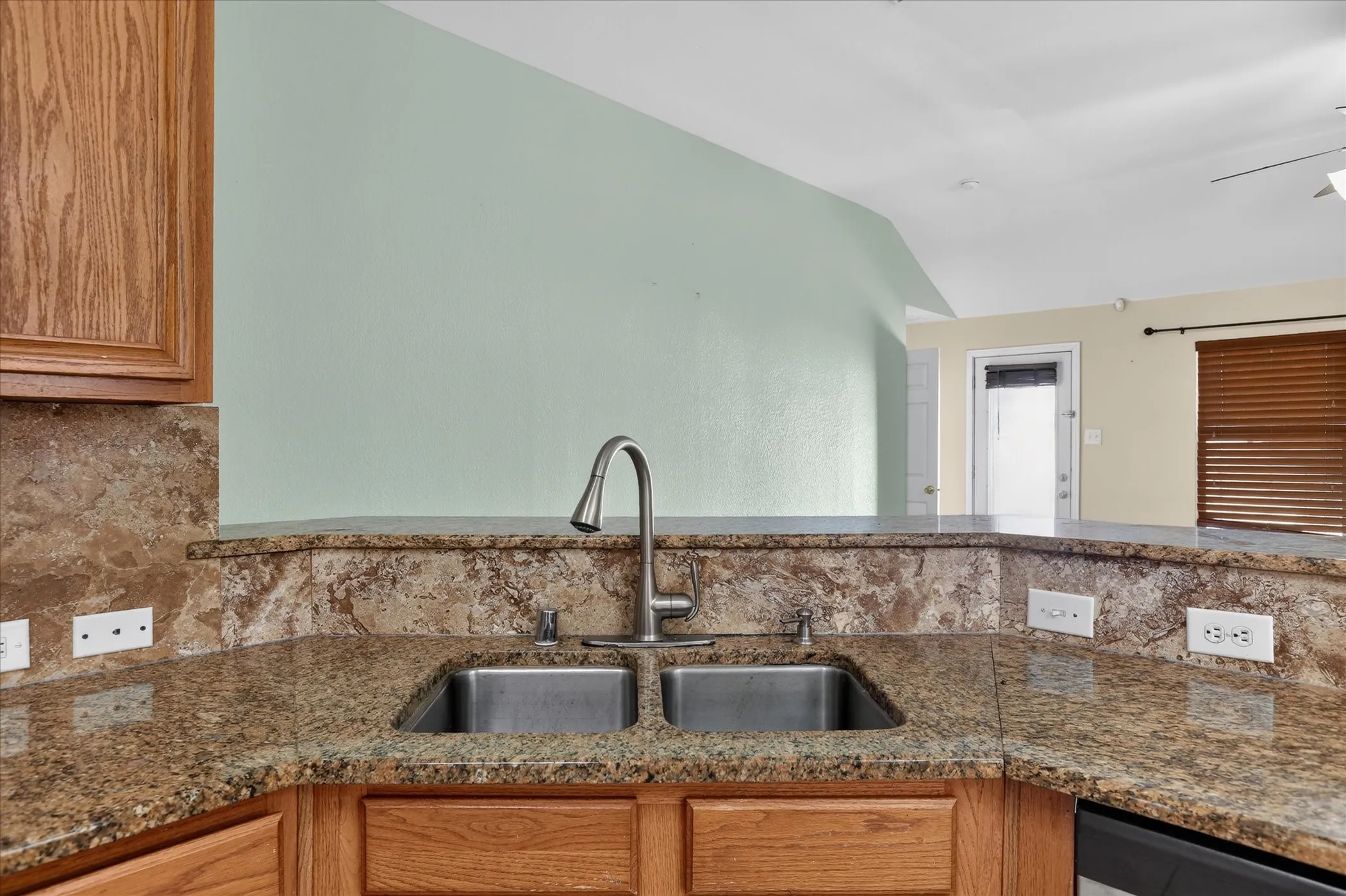 Granite countertops, stainless steel double basin sink, high-arc faucet, wood cabinetry, and a built-in dishwasher