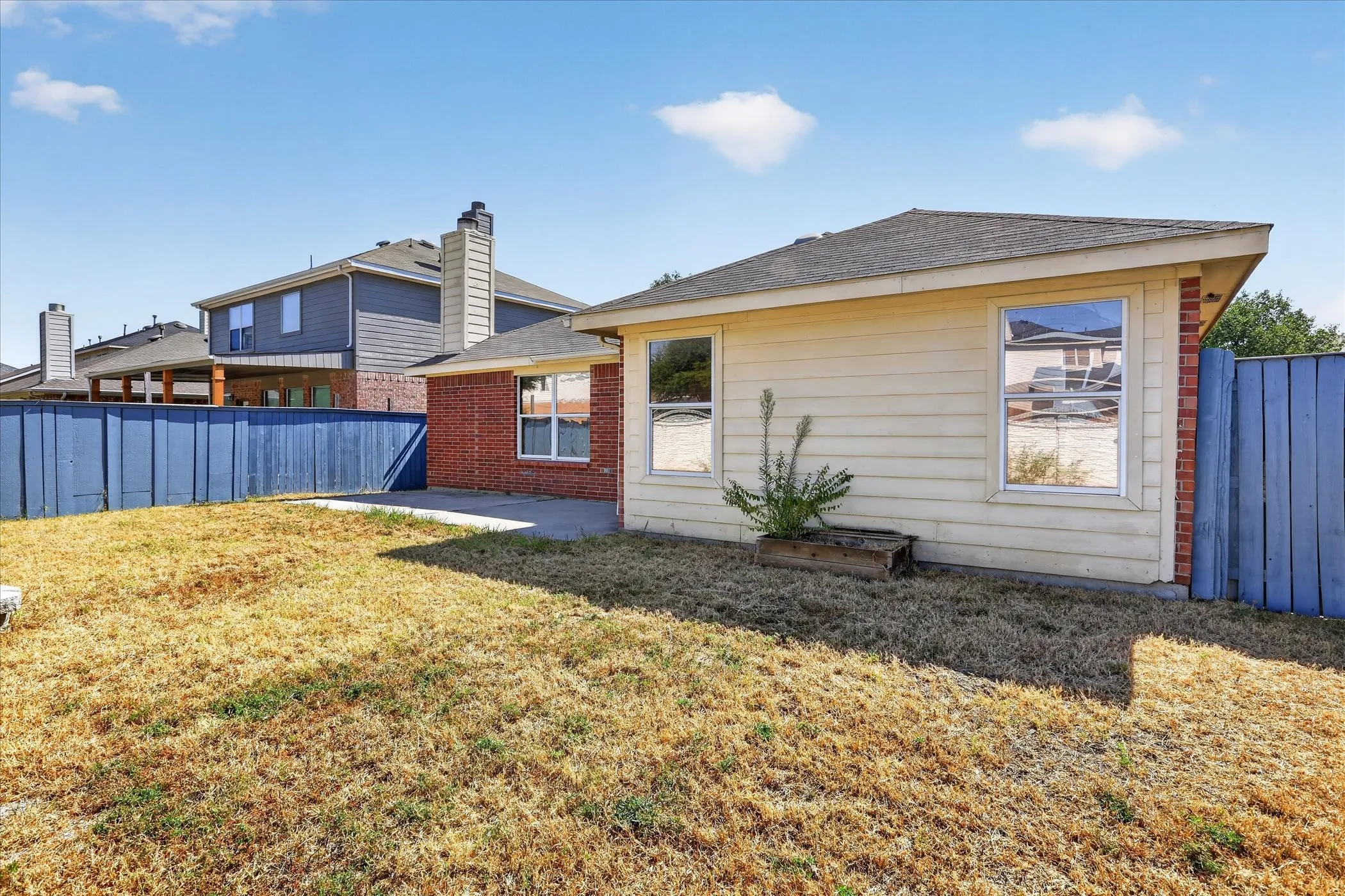 Exterior featuring brick and siding finishes, multiple windows, a concrete patio, and a blue privacy fence