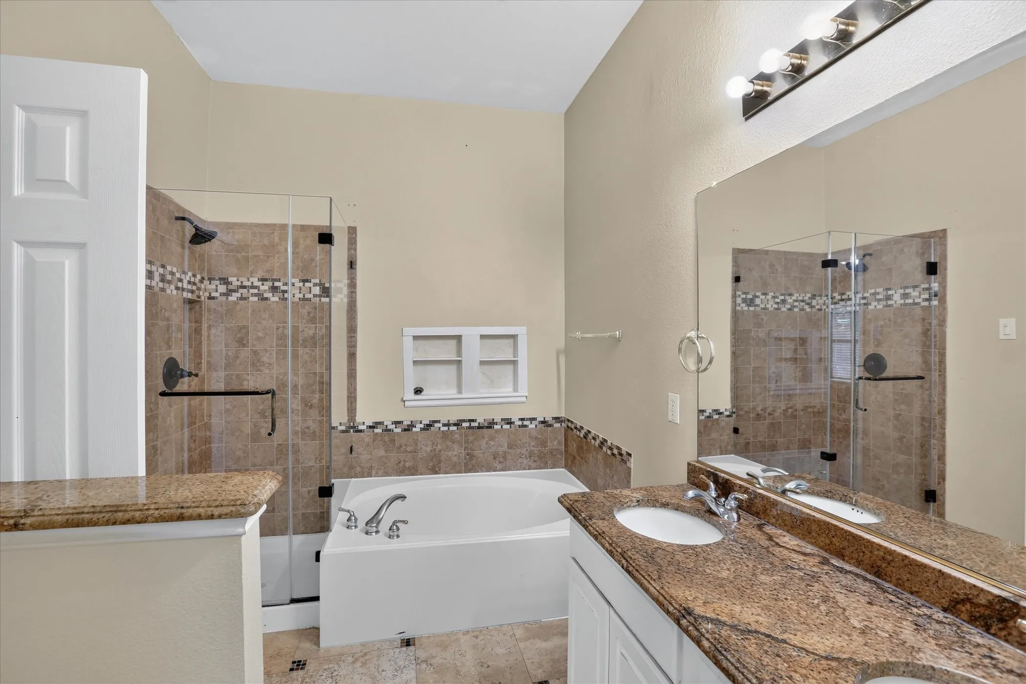 Dual vanity with stone countertops, walk-in shower with glass enclosure, separate soaking tub, and tile flooring