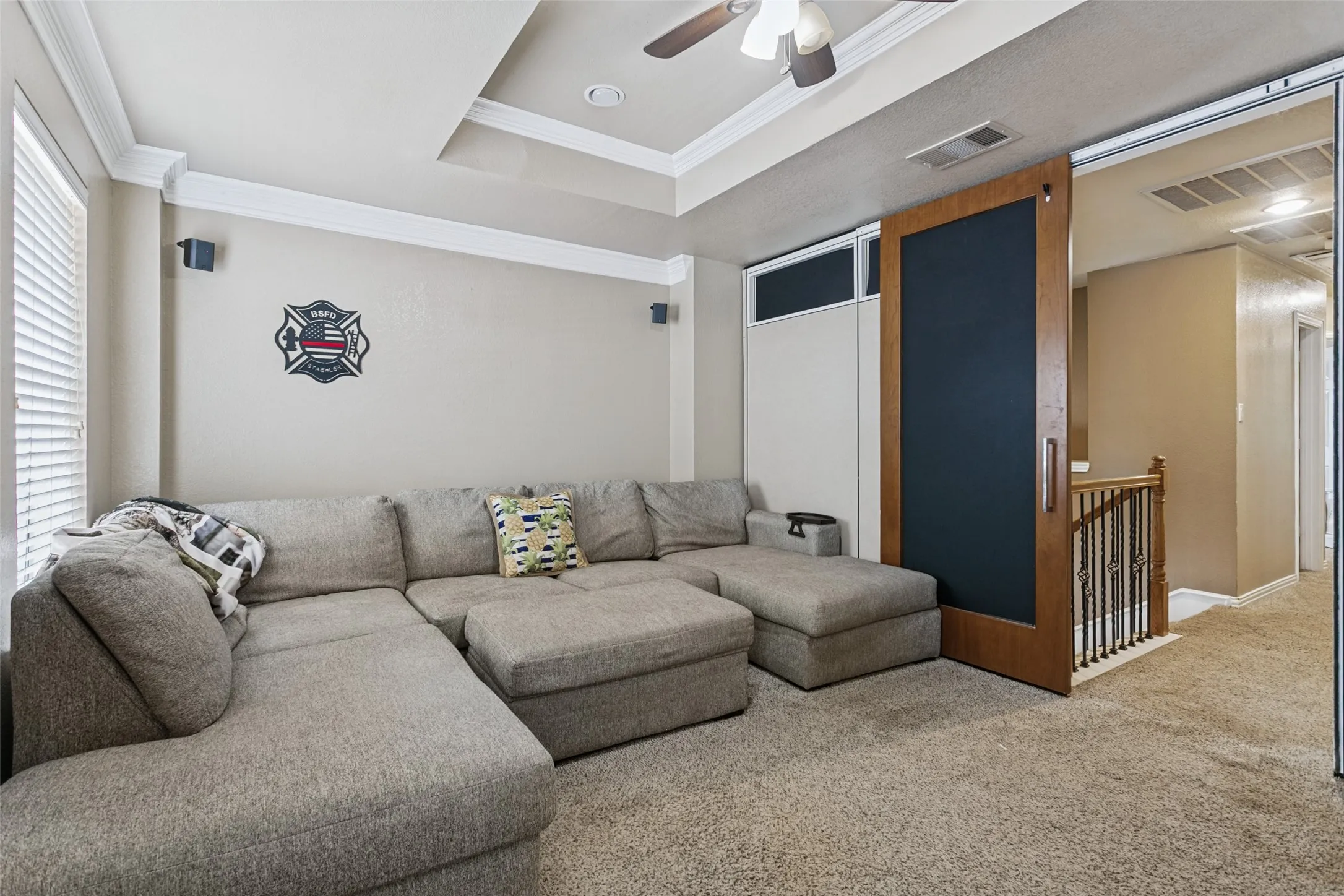 Tray ceiling with crown molding, ceiling fan, wood barn door, and carpet flooring