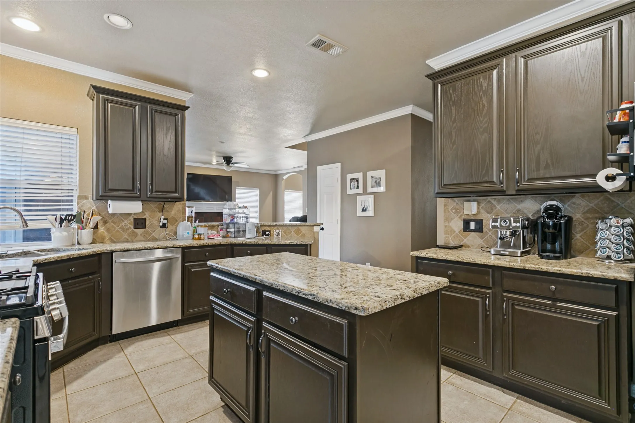 Kitchen featuring dark wood-finish cabinetry, light-toned granite countertops, a tiled backsplash, a central island, and stainless steel appliances