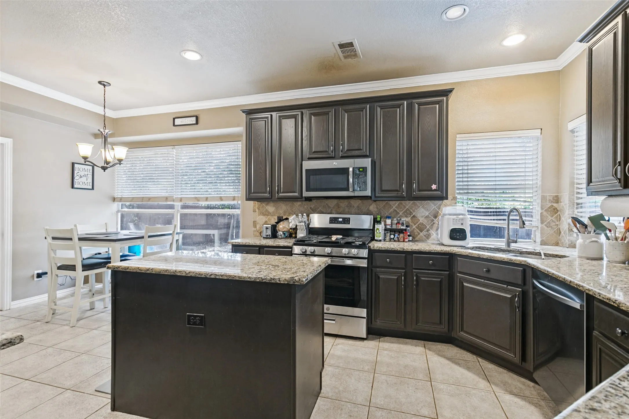 Spacious kitchen featuring dark wood cabinetry, granite countertops, stainless steel appliances, a tile backsplash, and recessed lighting