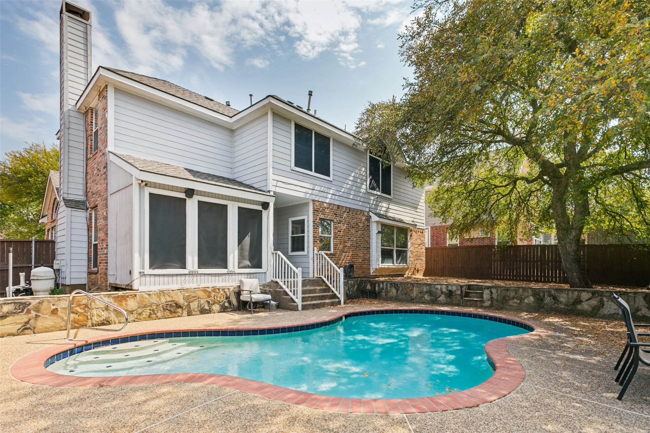Backyard with a freeform swimming pool, textured concrete decking, and stone retaining walls