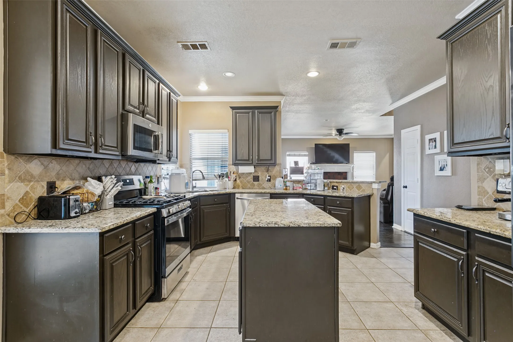 Kitchen featuring granite countertops, dark wood cabinetry, tile flooring, stainless steel appliances, and a tile backsplash