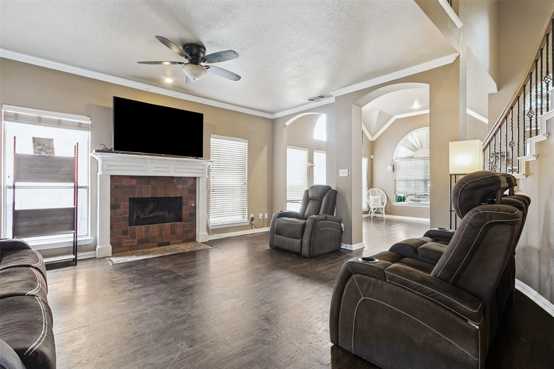 Spacious living area featuring wood-finish flooring, a brick fireplace with a white mantel, and ceiling fan