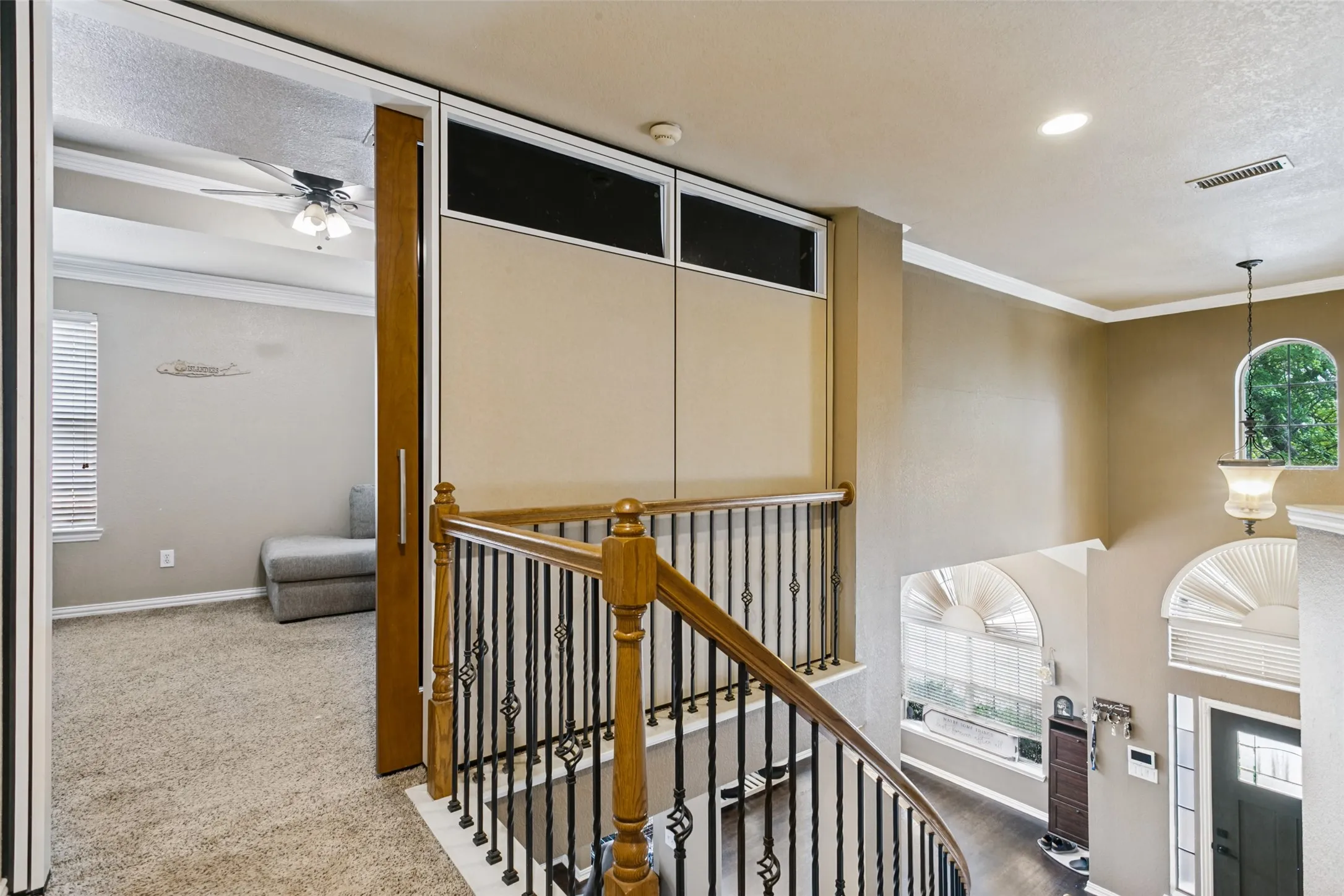 Wood-finish staircase with wrought iron balusters, crown molding, a recessed ceiling light, and a decorative pendant light