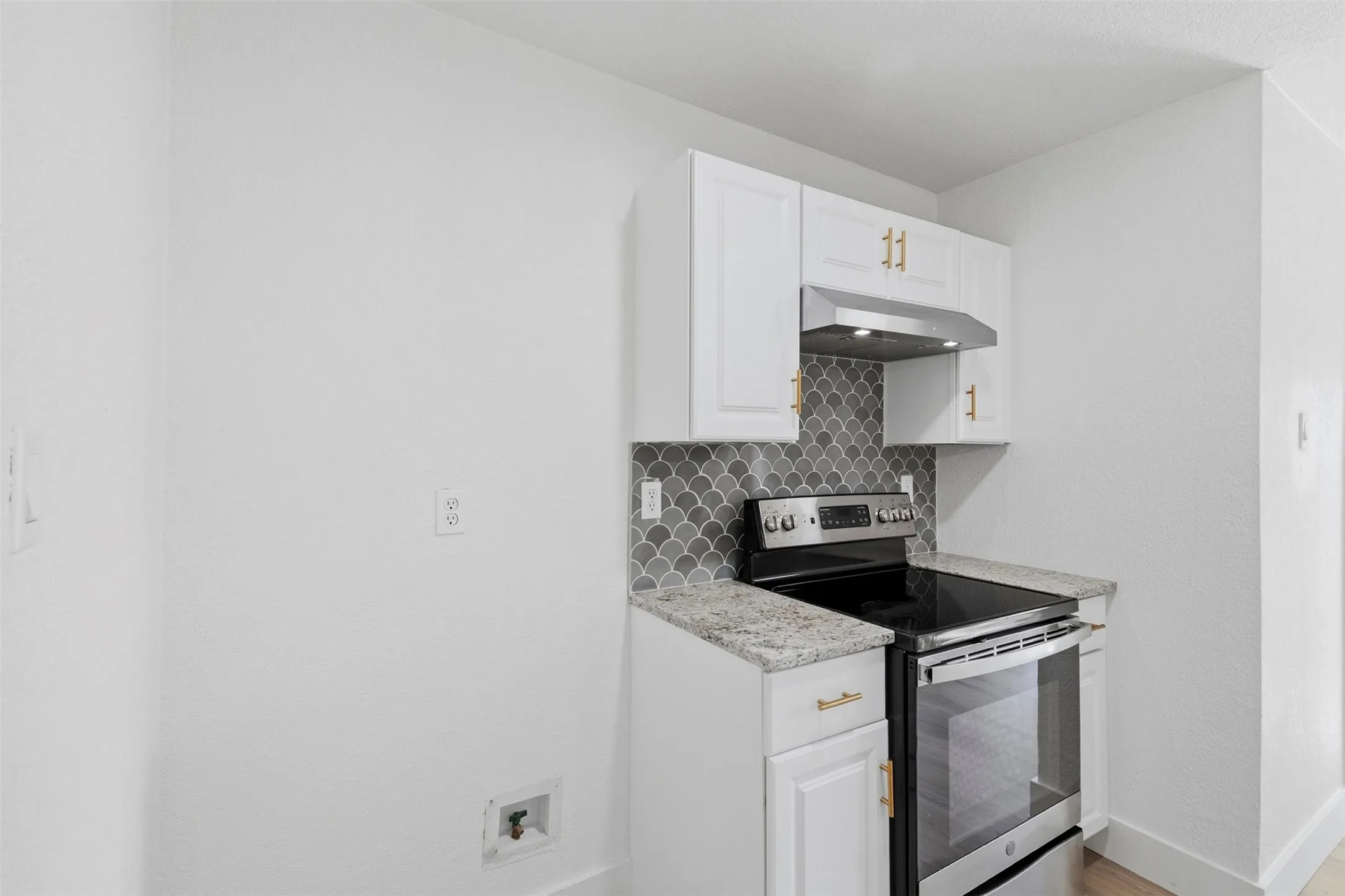 White cabinetry with gold-tone hardware, stainless steel electric range, granite-style countertops, and gray scallop-patterned tile backsplash
