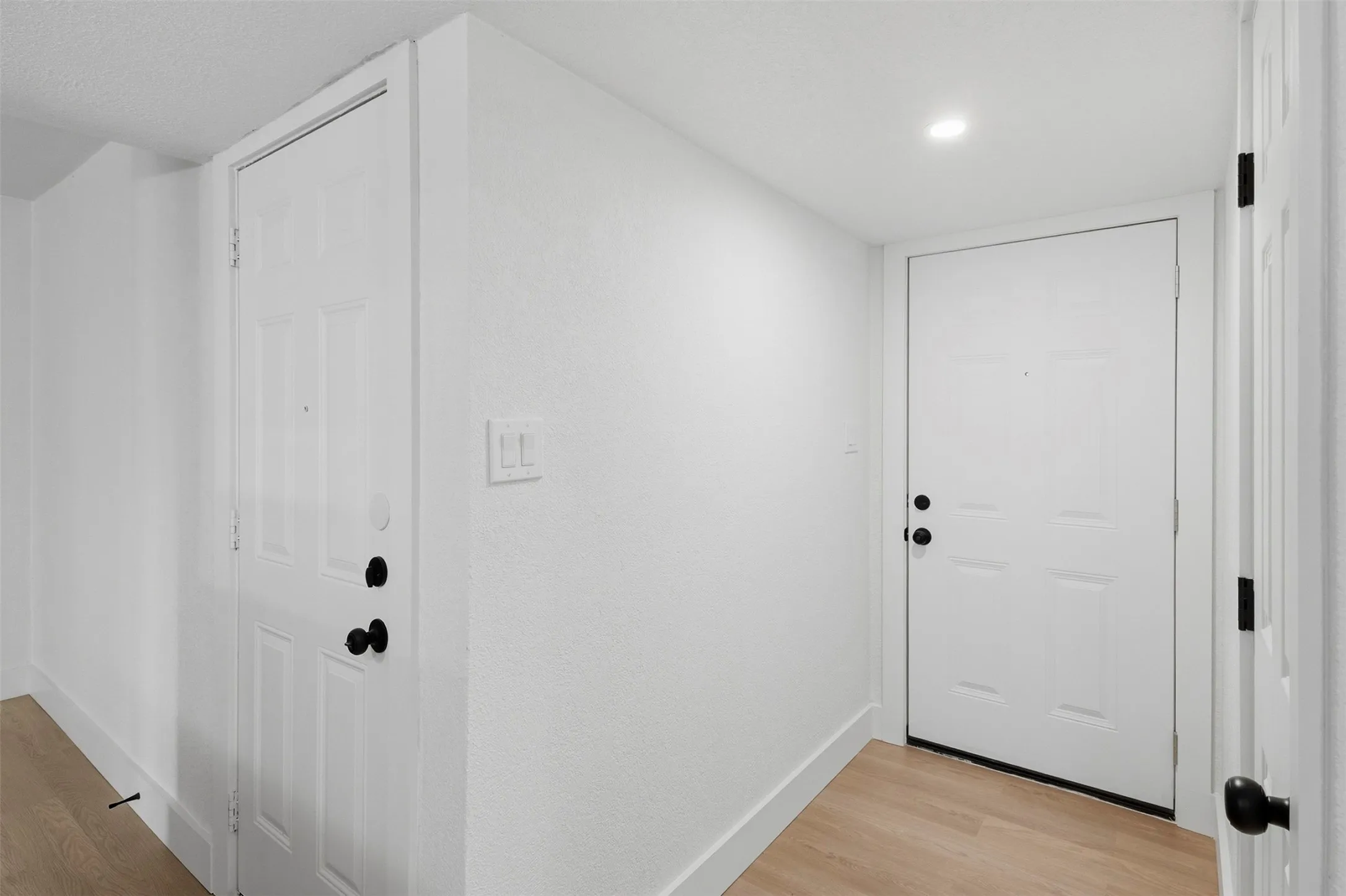 Recessed ceiling lighting, wood-finish flooring, white panel doors, black door hardware, and white wall finishes
