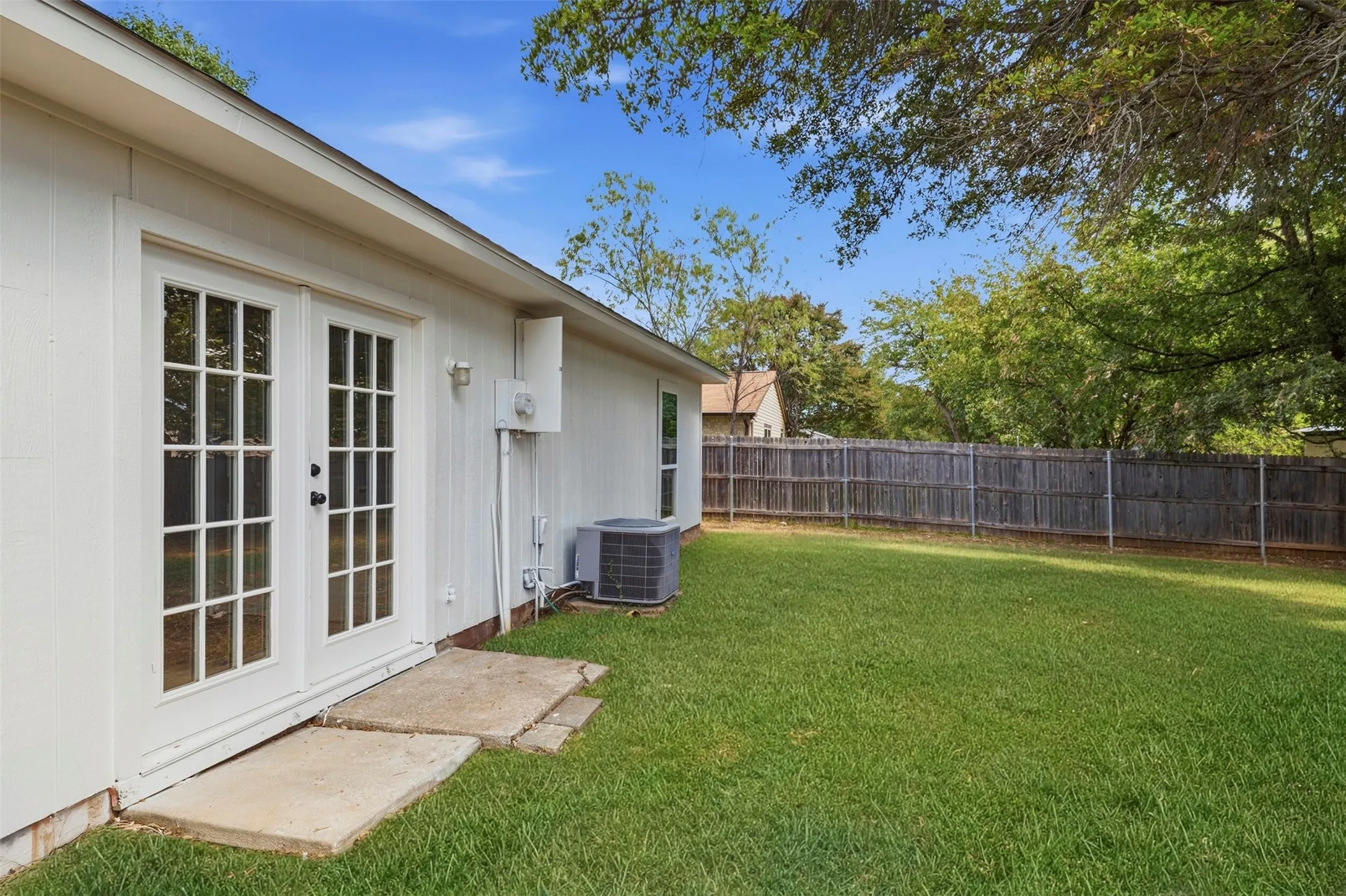 Greened yard featuring a wooden privacy fence, mature trees, and a white exterior with French doors