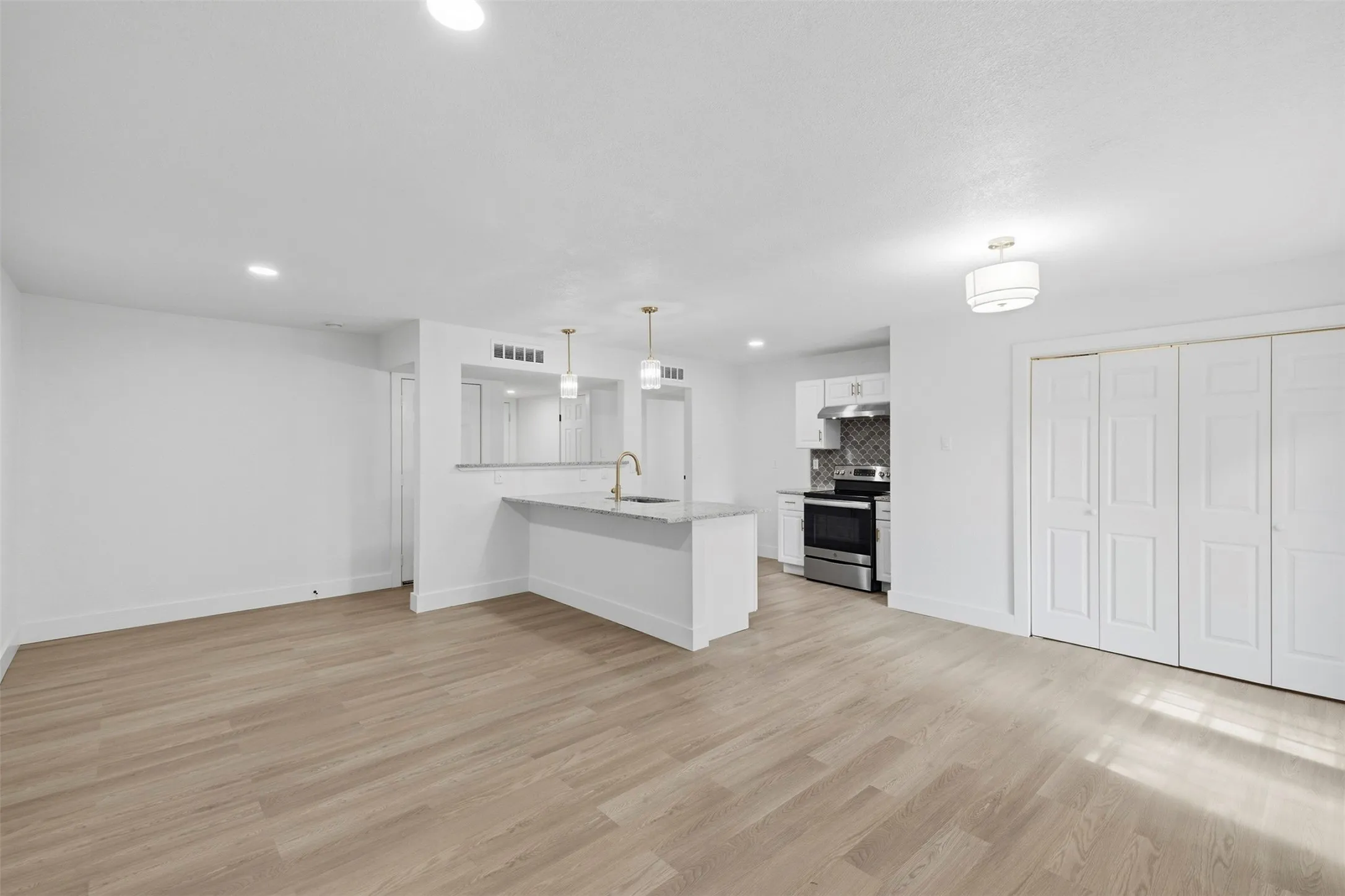 Open-concept living area featuring wood-finish flooring, recessed lighting, and a kitchen island with pendant lighting