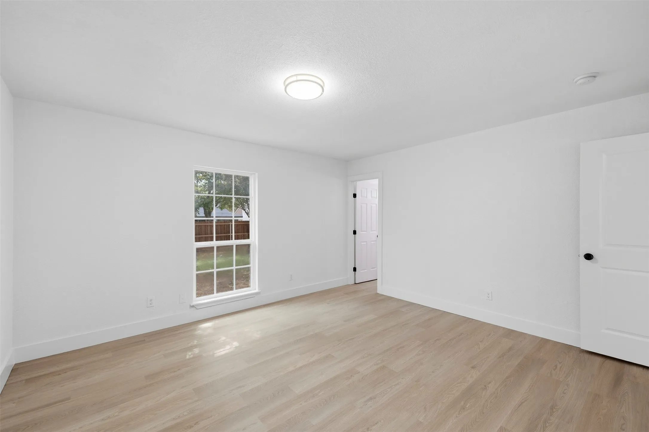 Light wood-finish flooring, white walls, and a multi-pane window