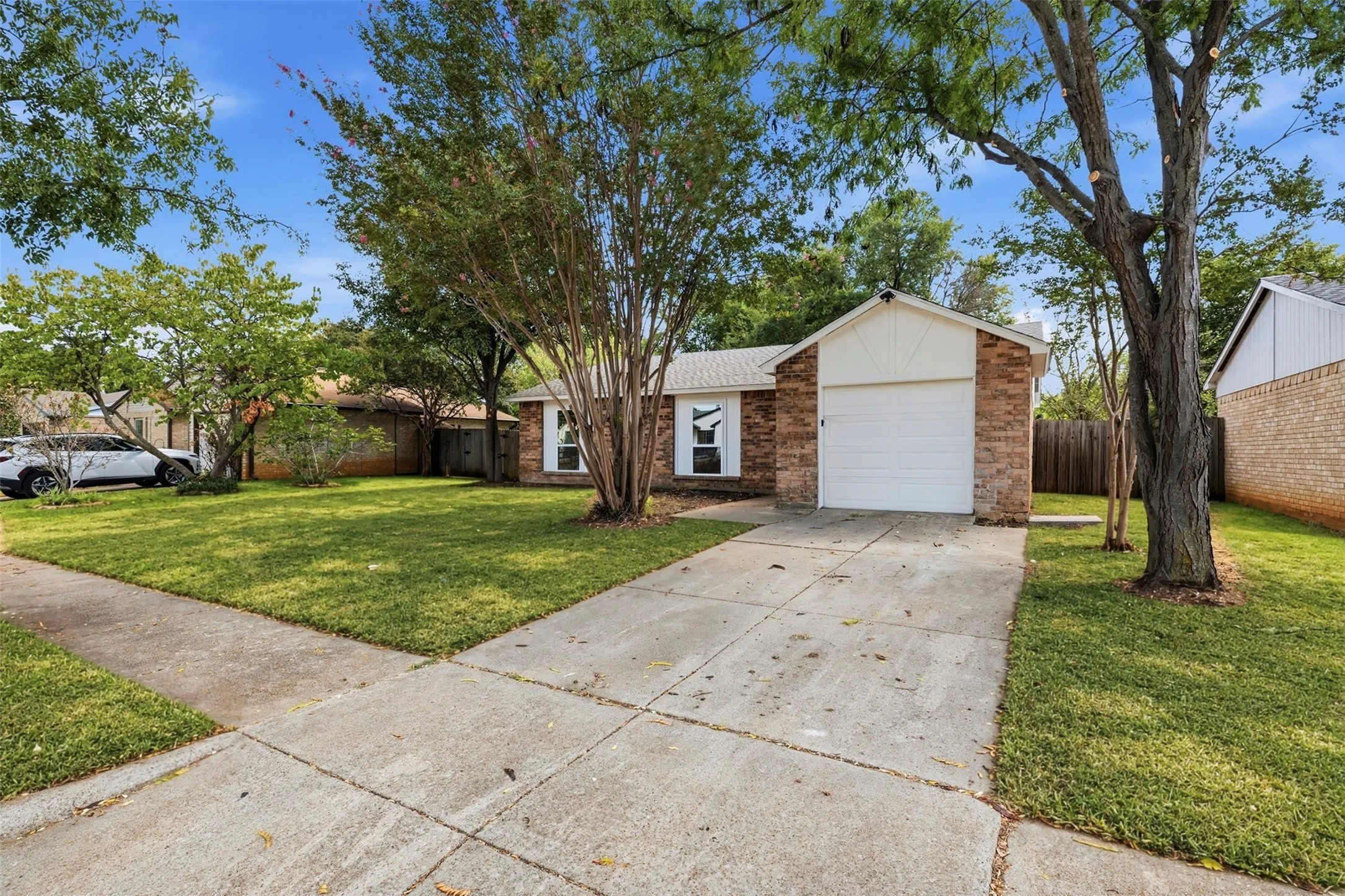 Brick facade with white siding accents, an attached garage, and a concrete driveway
