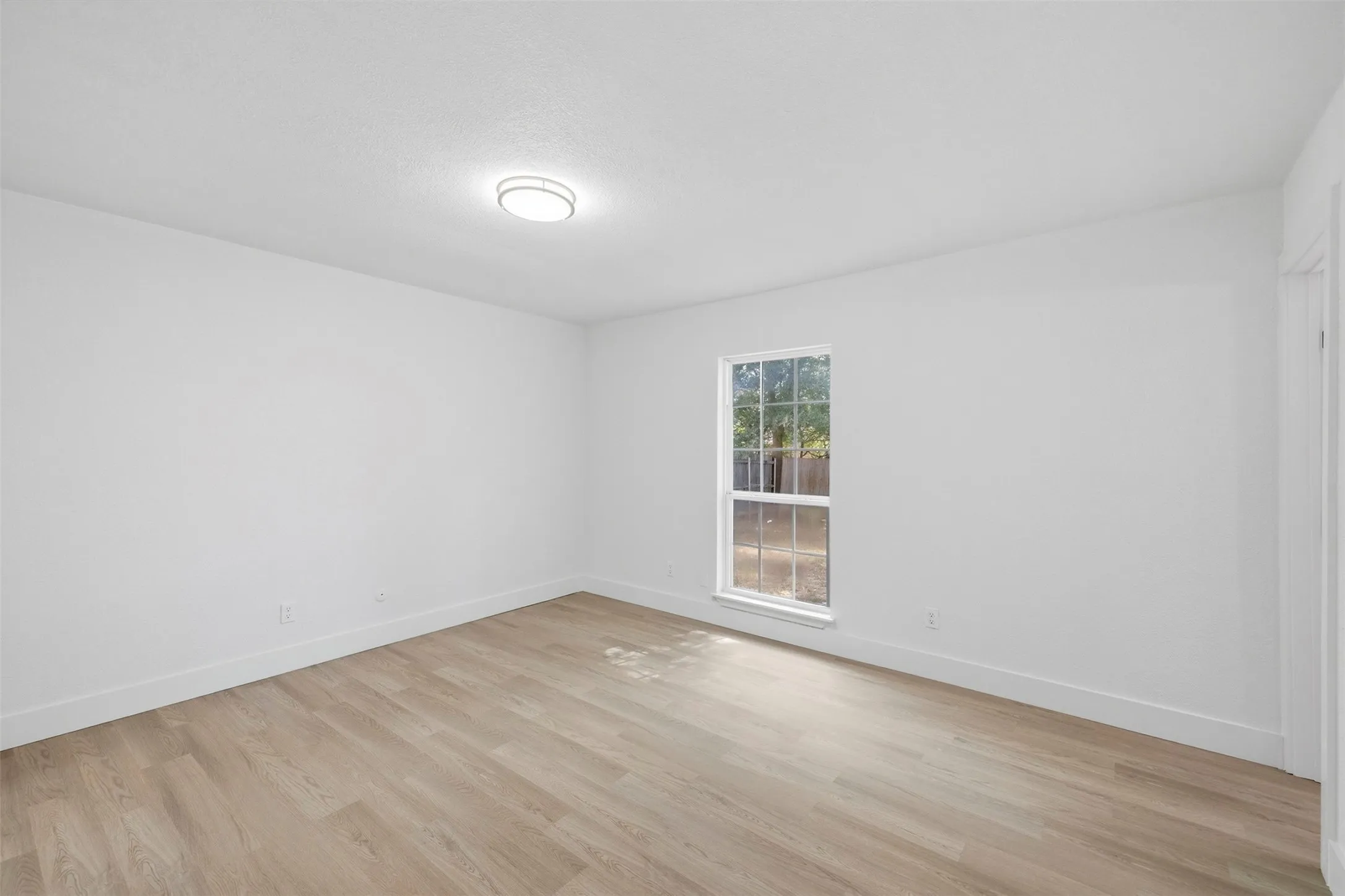 Wood-finish flooring, single window, white walls, and a ceiling-mounted light fixture