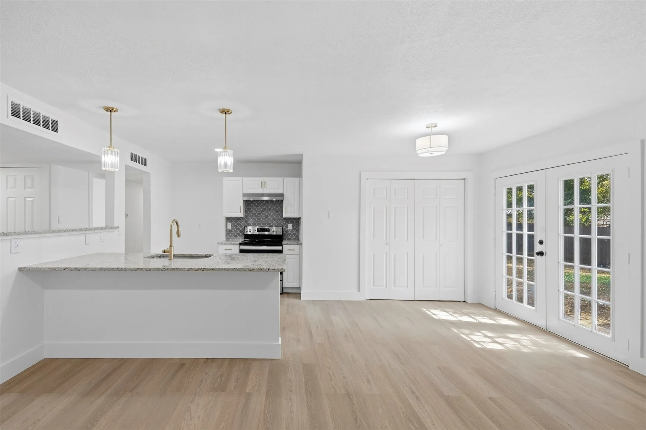 Wood-finish flooring, white cabinetry, granite countertops, stainless steel appliances, and French doors