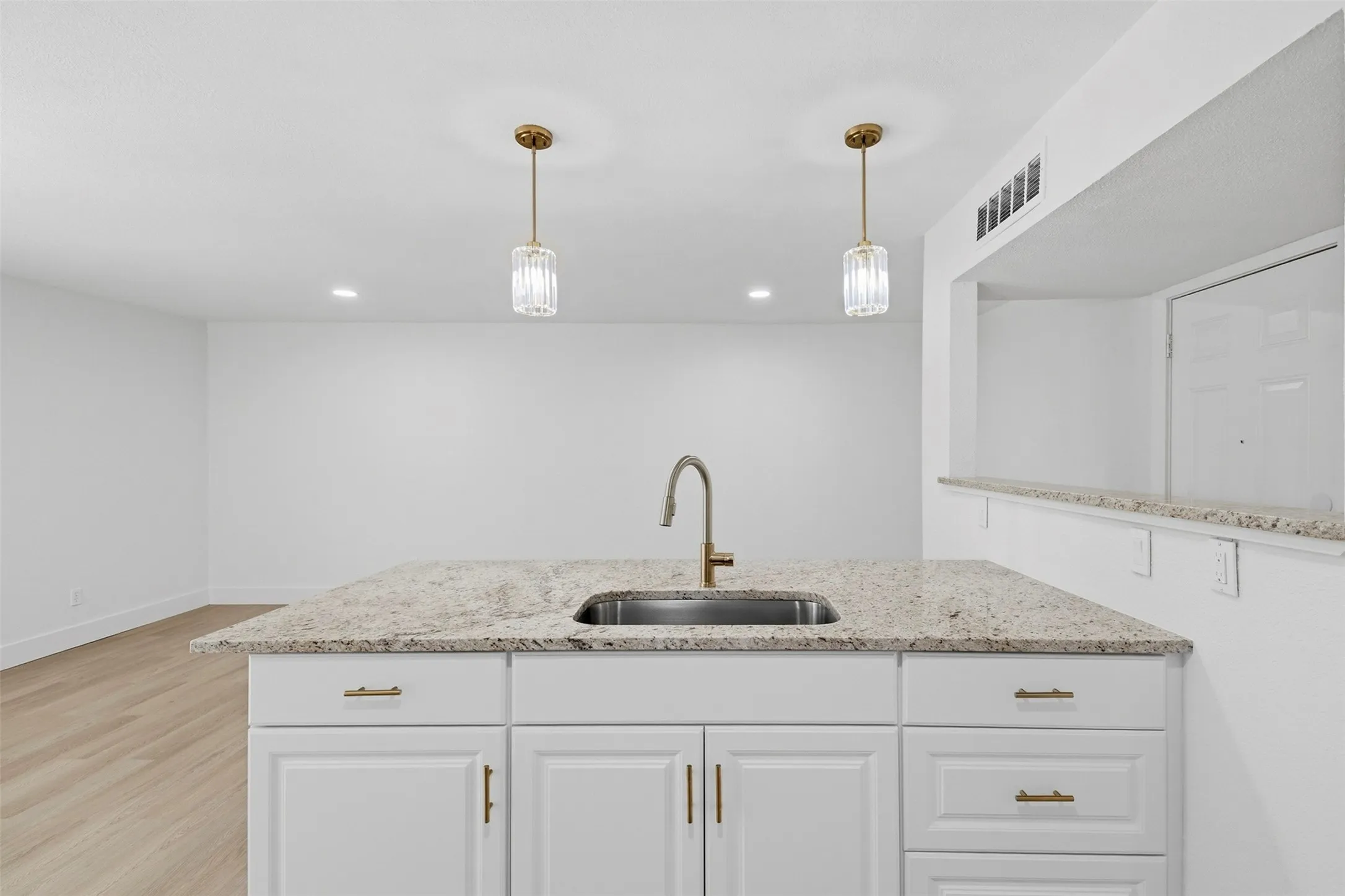 Kitchen island with a stainless steel undermount sink, granite countertop, and white cabinetry with gold-toned hardware