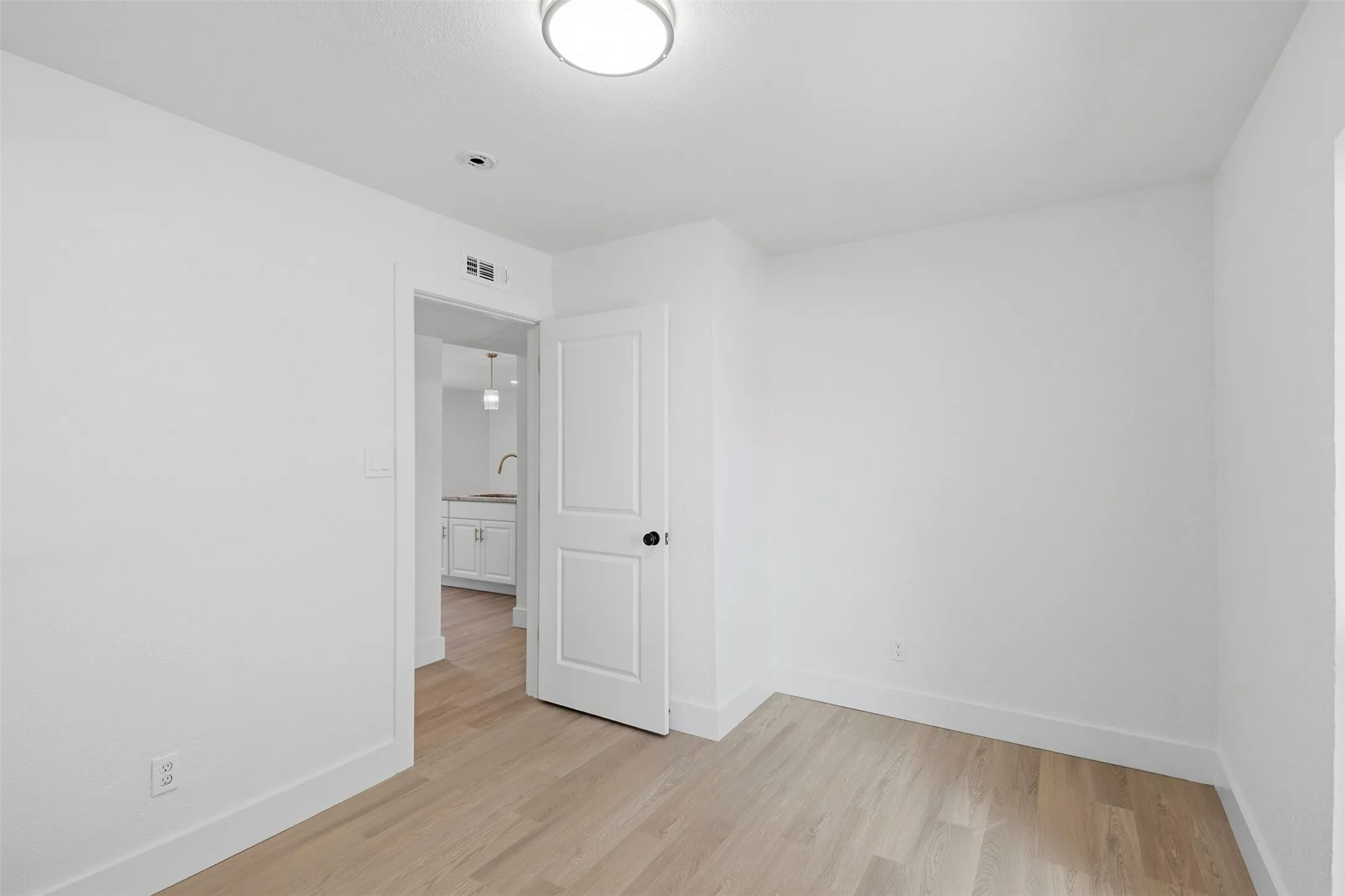 Recessed ceiling light, wood-finish flooring, white walls, white trim, white interior door with black hardware