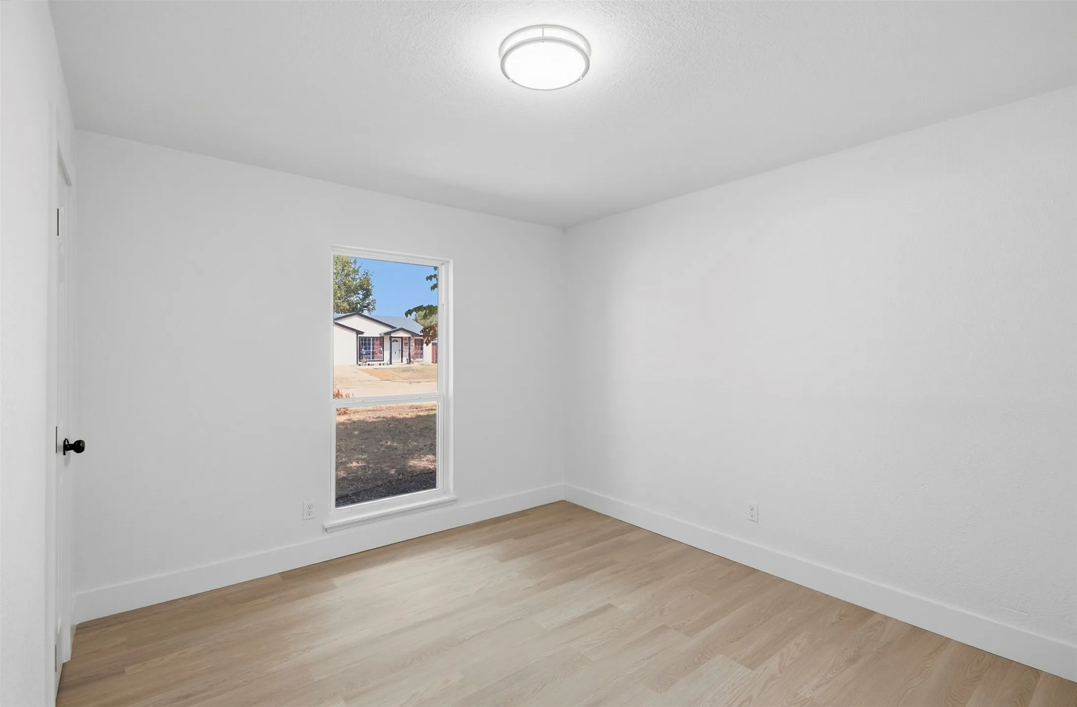 Light-toned wood-finish flooring, white walls, and a single window with white trim
