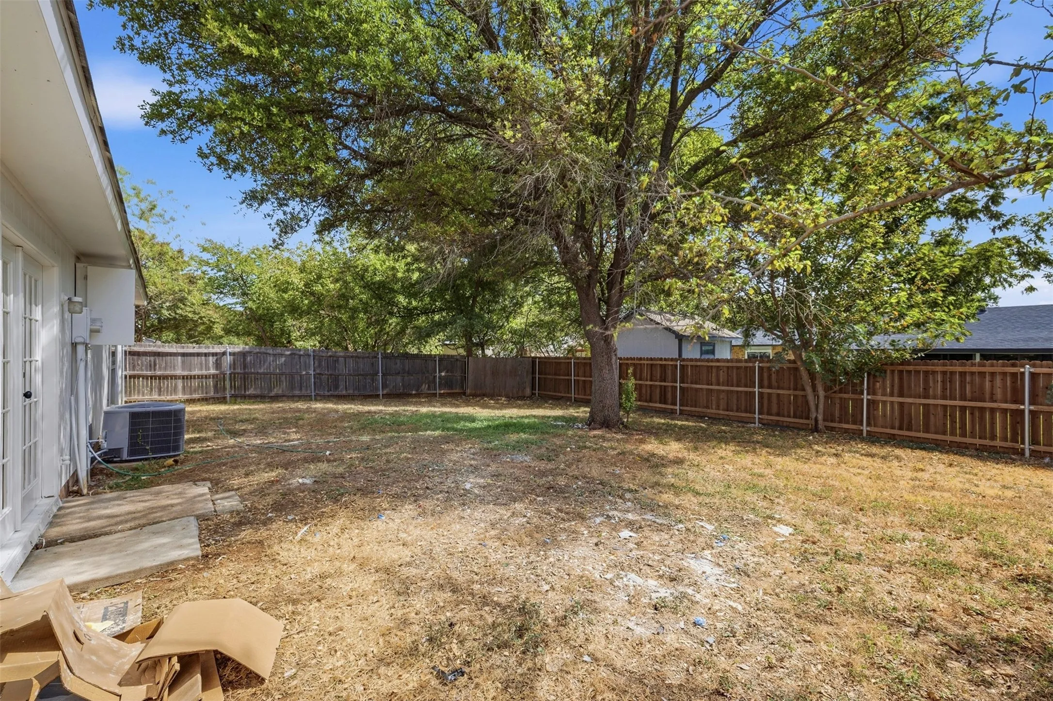 Expansive backyard with a wood privacy fence, mature trees, and a glass-paneled exterior door