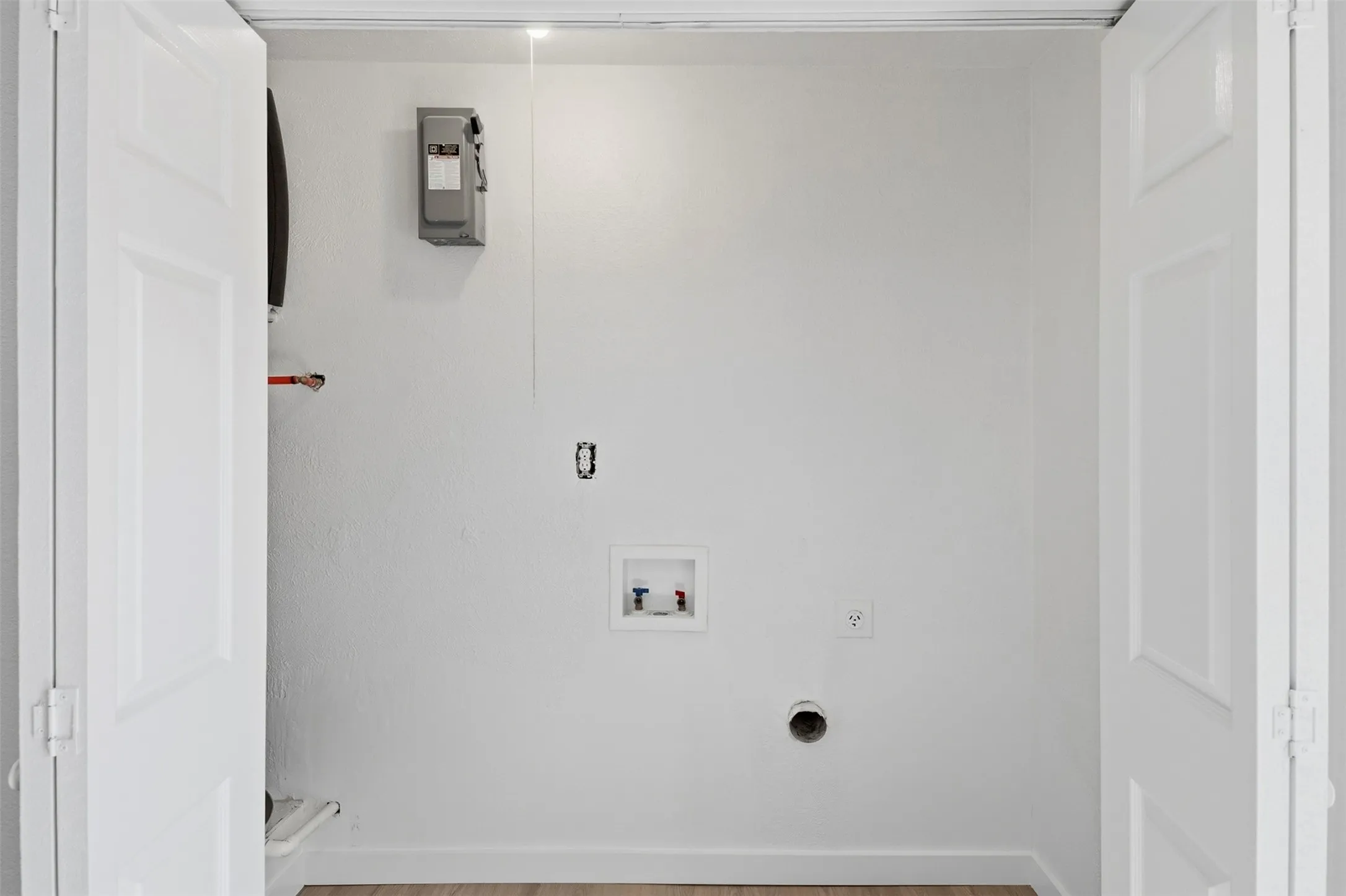 Laundry hookups with white walls and wood-finish flooring