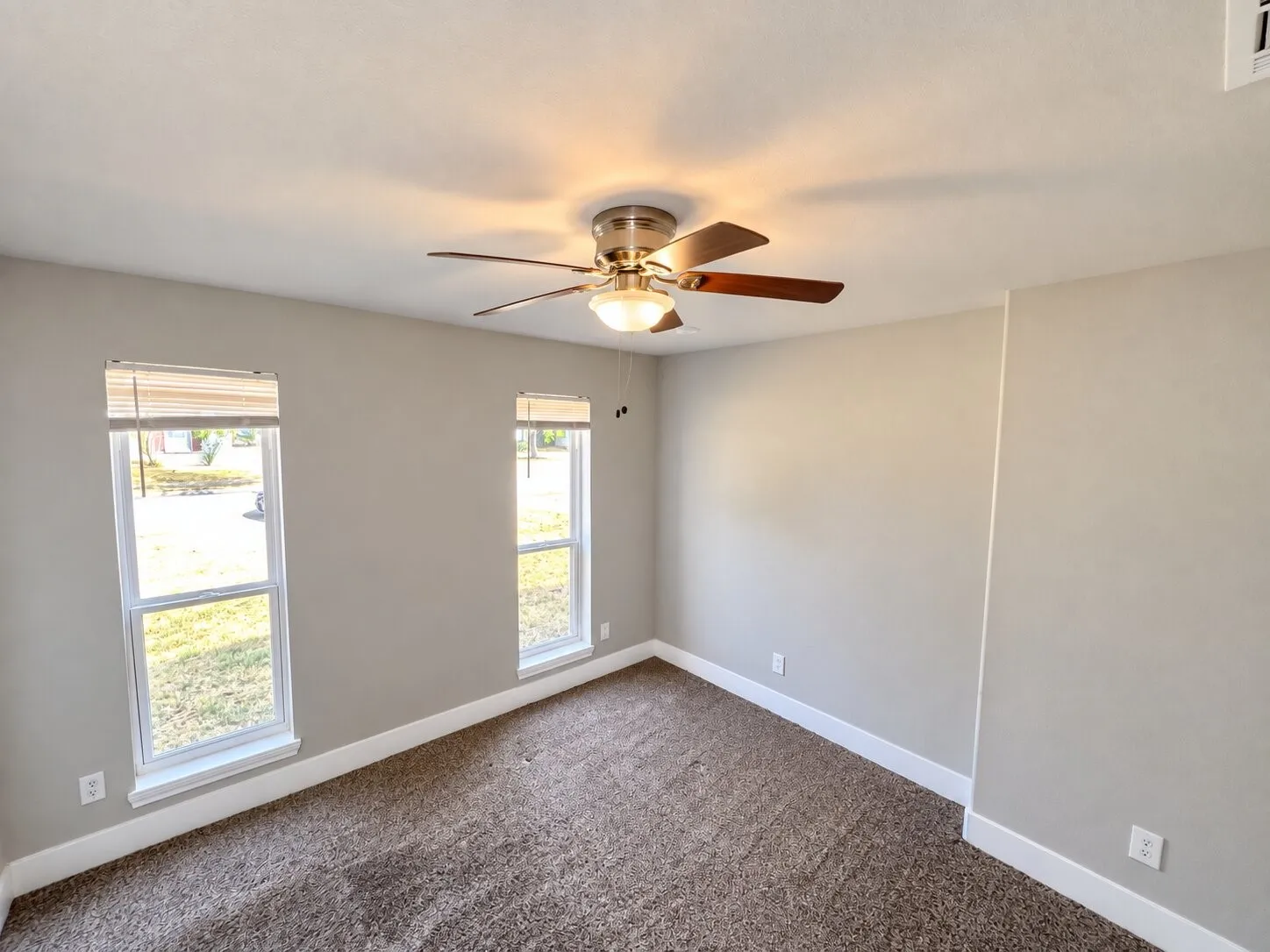 Neutral-toned wall finish, recessed windows, textured carpet flooring, ceiling fan with integrated lighting, and crisp white baseboards