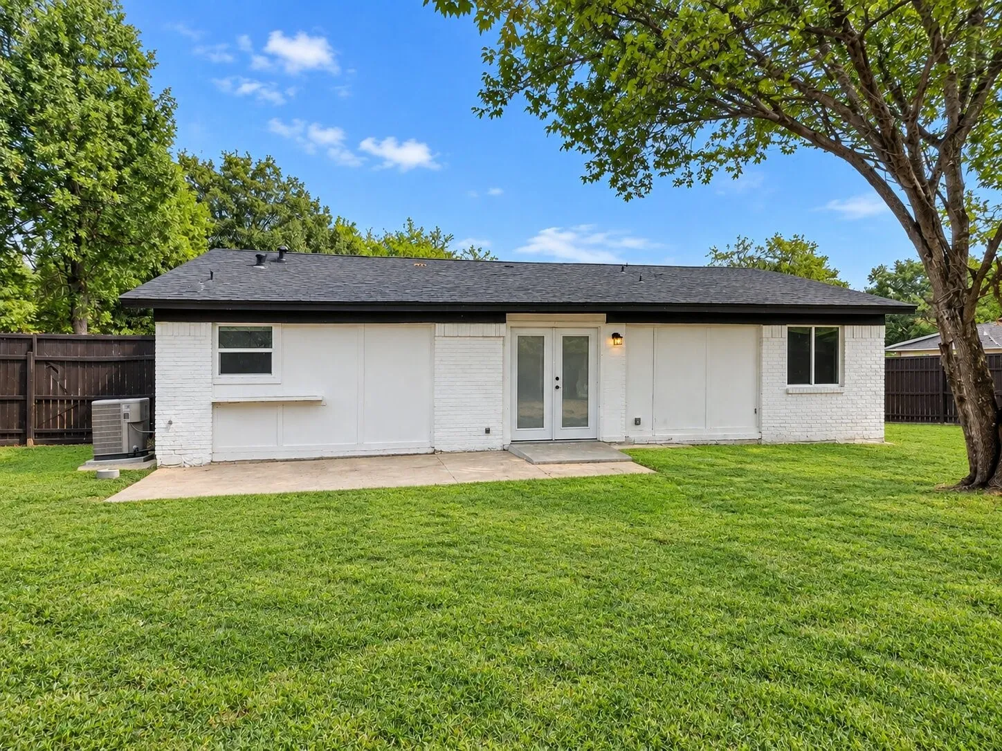 Expansive backyard with a manicured lawn, concrete patio, and mature trees