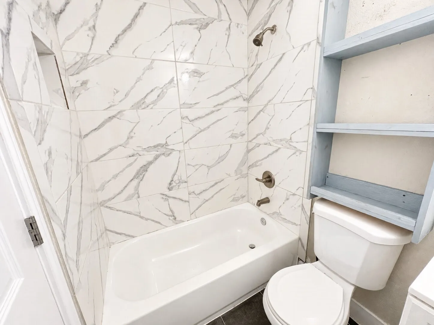 Bathroom featuring a white bathtub, toilet, tiled shower surround, and brushed bronze fixtures