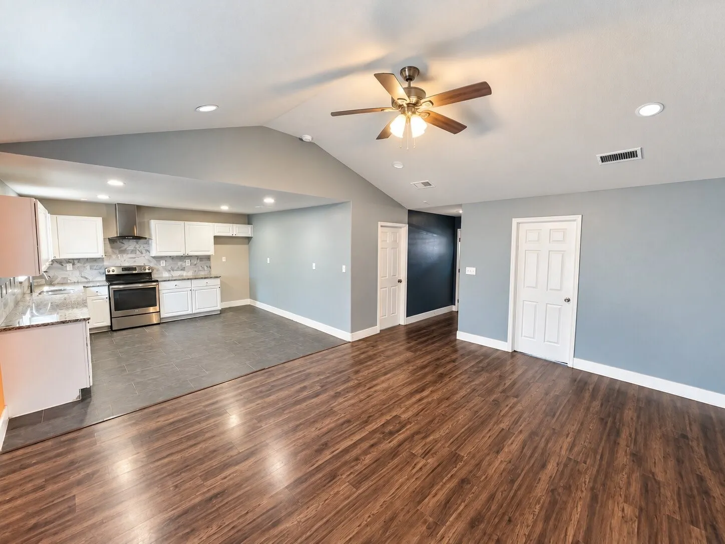 Open-concept living space featuring wood-finish flooring, a vaulted ceiling with a ceiling fan, and recessed lighting