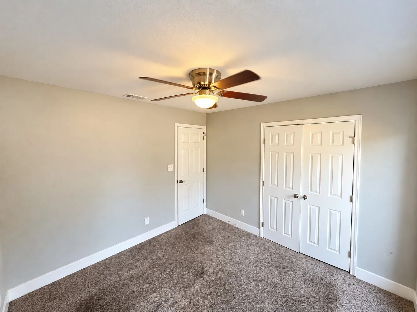 Neutral-toned walls, textured carpeting, ceiling fan with light fixture, paneled doors, and white trim