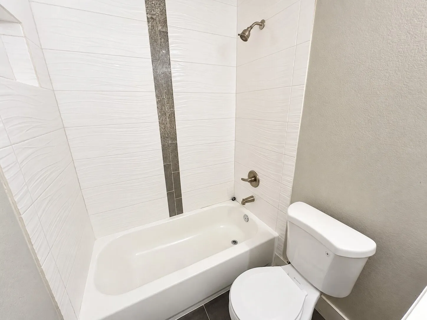 Bathtub with white subway tile surround, textured accent tile inlay, and brushed nickel fixtures