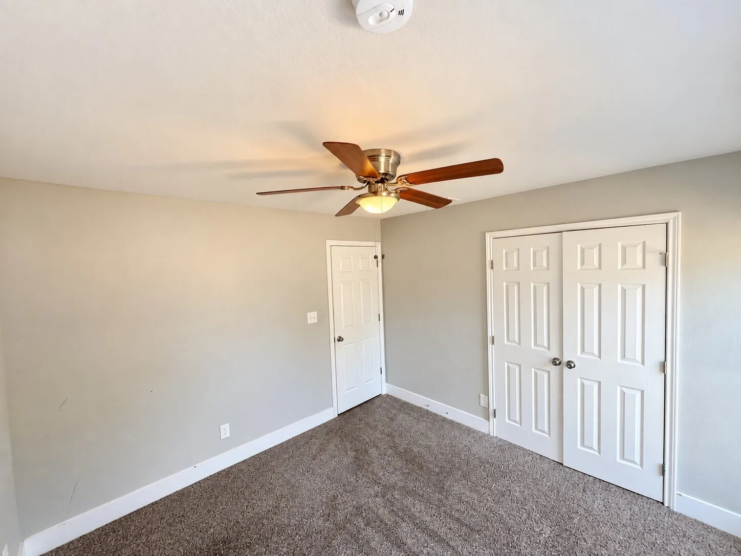 Neutral wall paint with carpeted flooring, a ceiling fan with integrated lighting, and white paneled doors