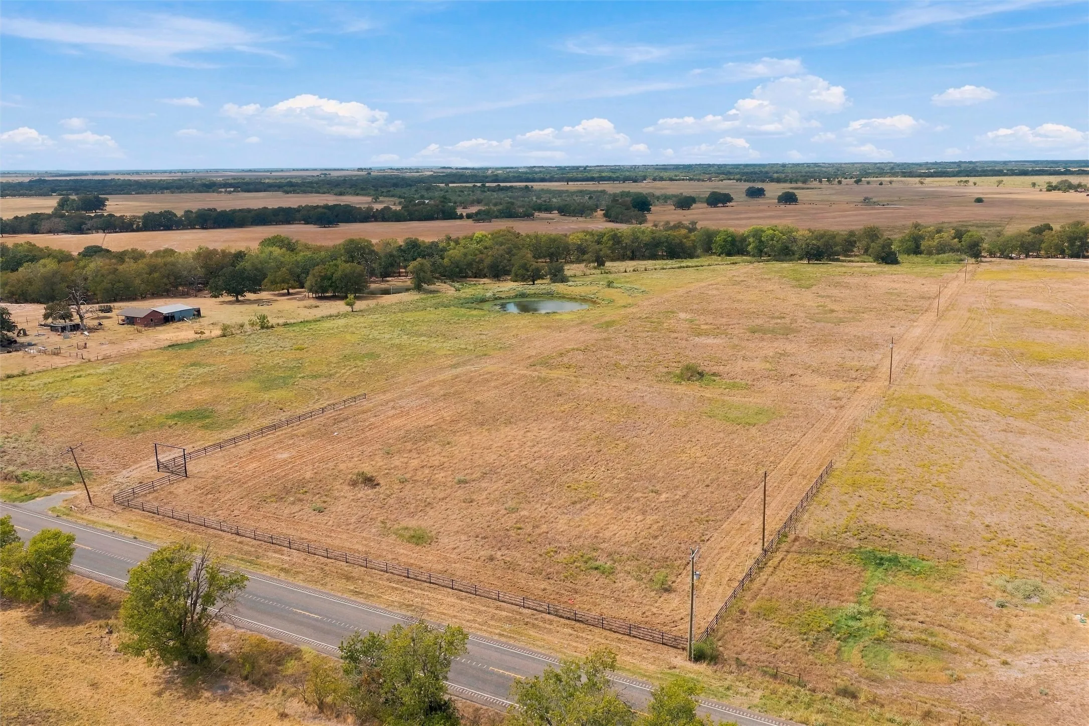 Expansive acreage with perimeter fencing, a private pond, and tree-lined boundaries