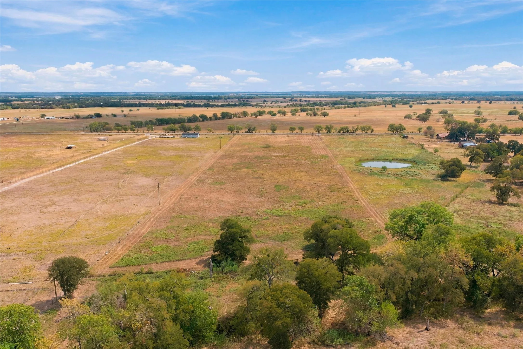Expansive rural property featuring an established pond, scattered mature trees, and a distant residential structure