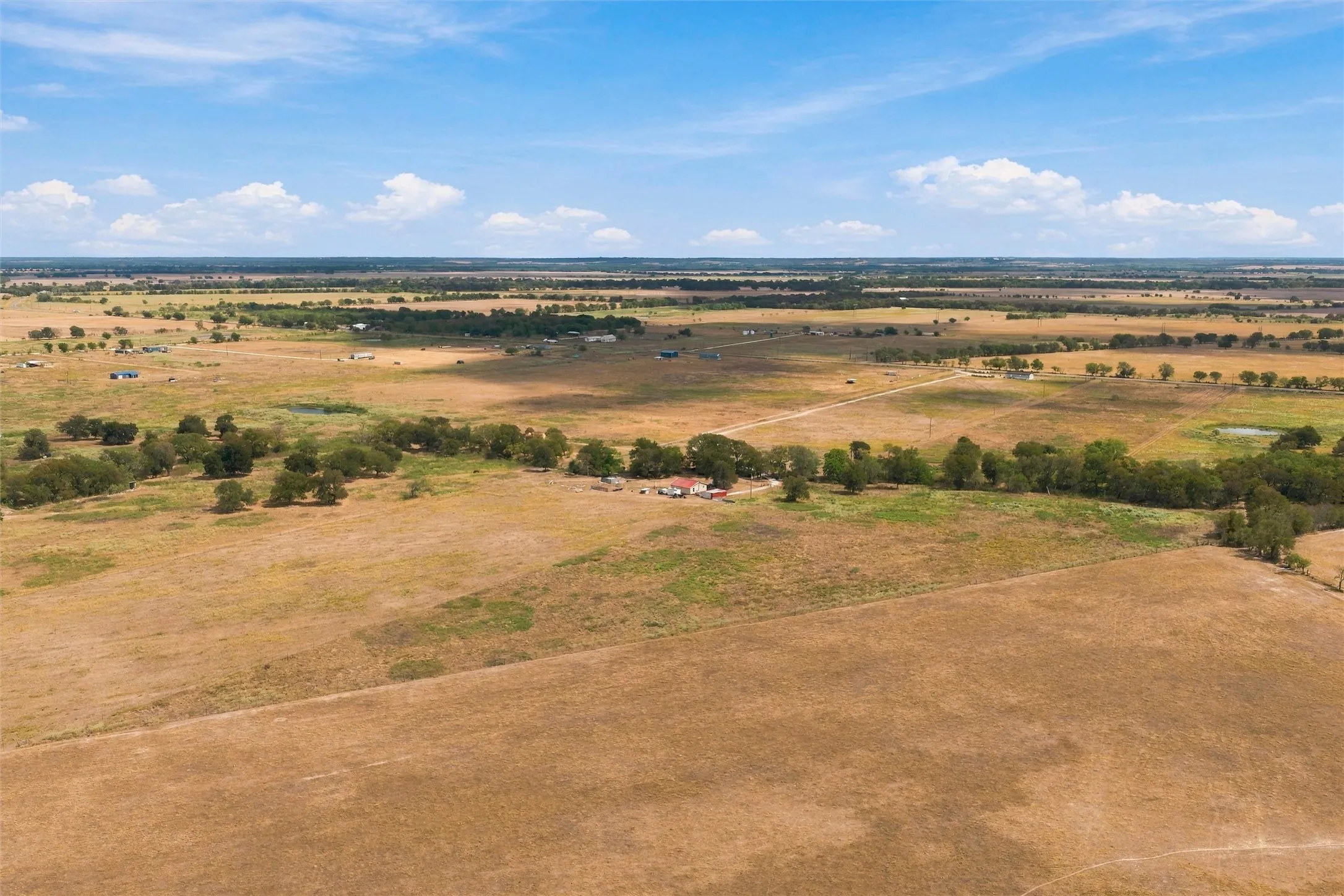 Expansive property featuring vast open fields, scattered mature trees, and a distant building cluster