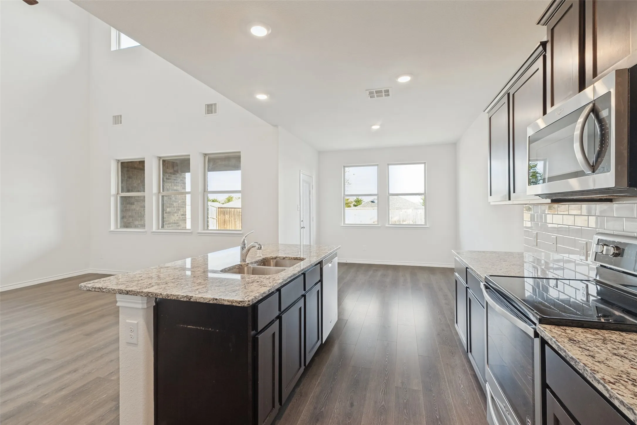 Kitchen island with dual sinks, granite countertops, and dark wood cabinetry