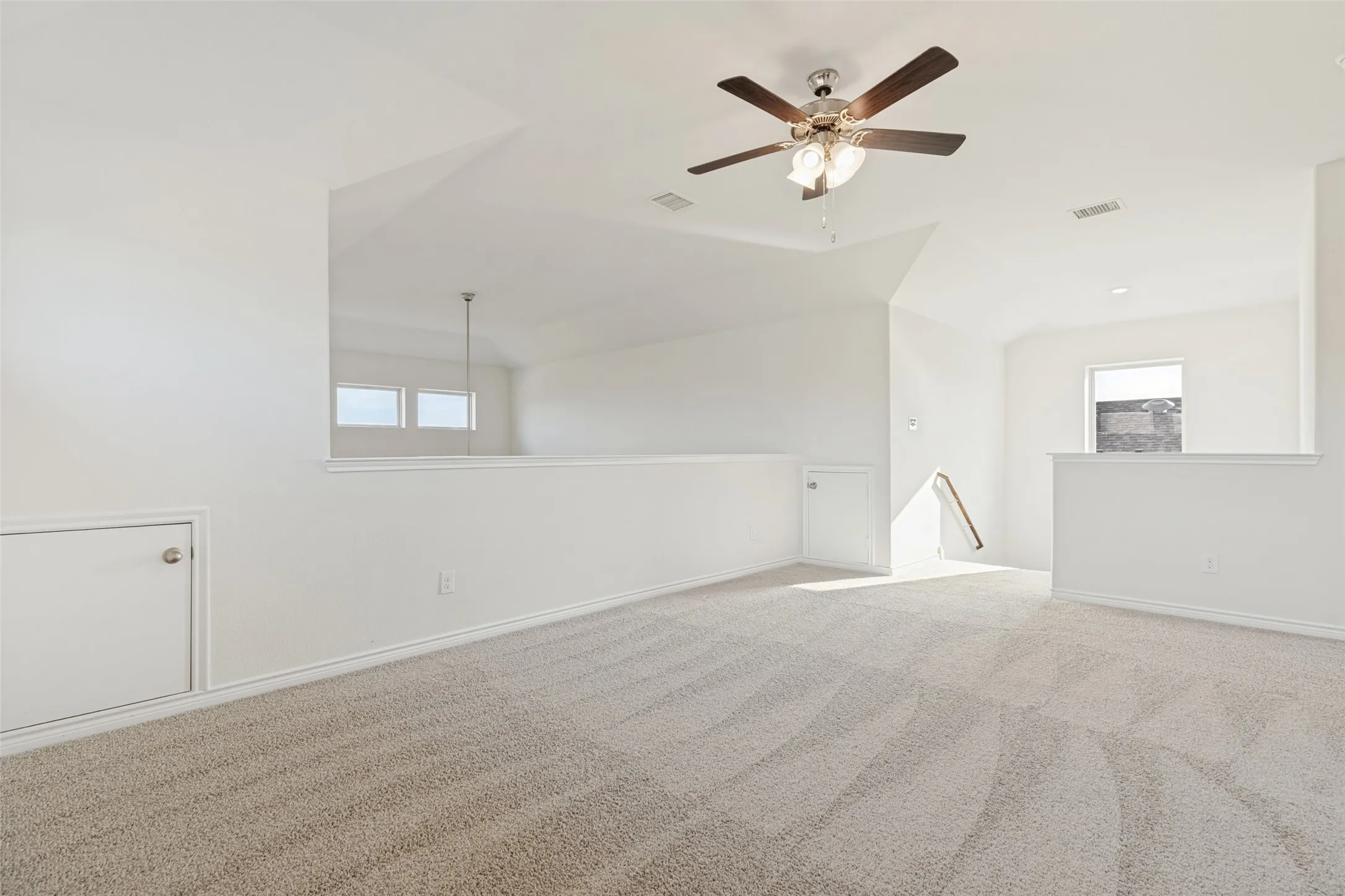 Carpeted loft space featuring sloped ceilings, a ceiling fan, and built-in storage access