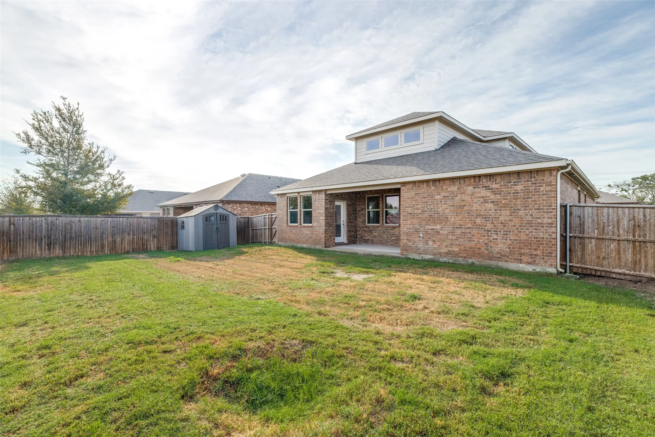 Expansive backyard featuring a wood privacy fence, brick exterior, and a dormer with multiple windows