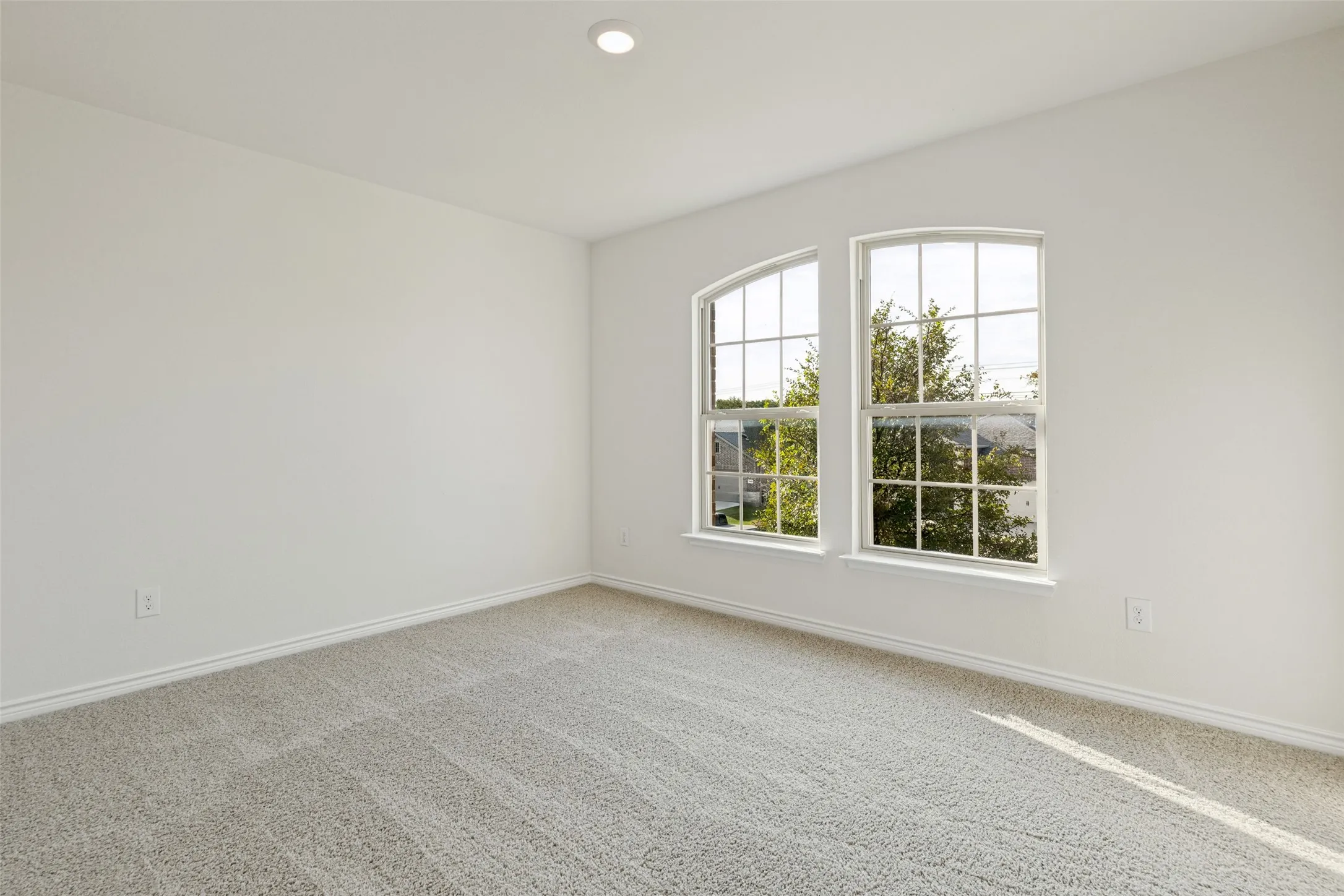 Light-toned walls, recessed ceiling lighting, two arched transom windows, and light-toned carpeting