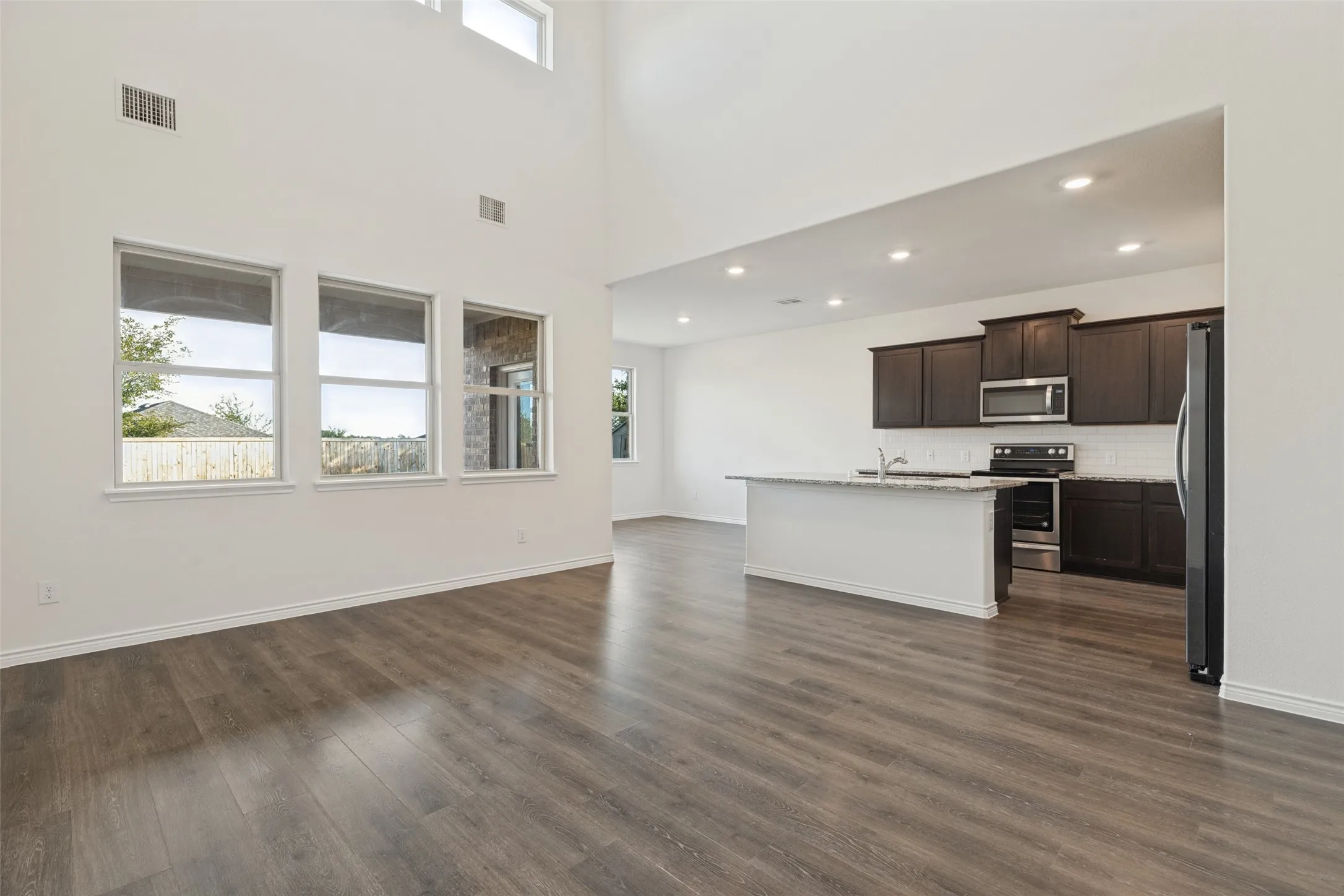 Two-story ceiling, wood-finish flooring, kitchen island, dark wood cabinetry, and stainless steel appliances