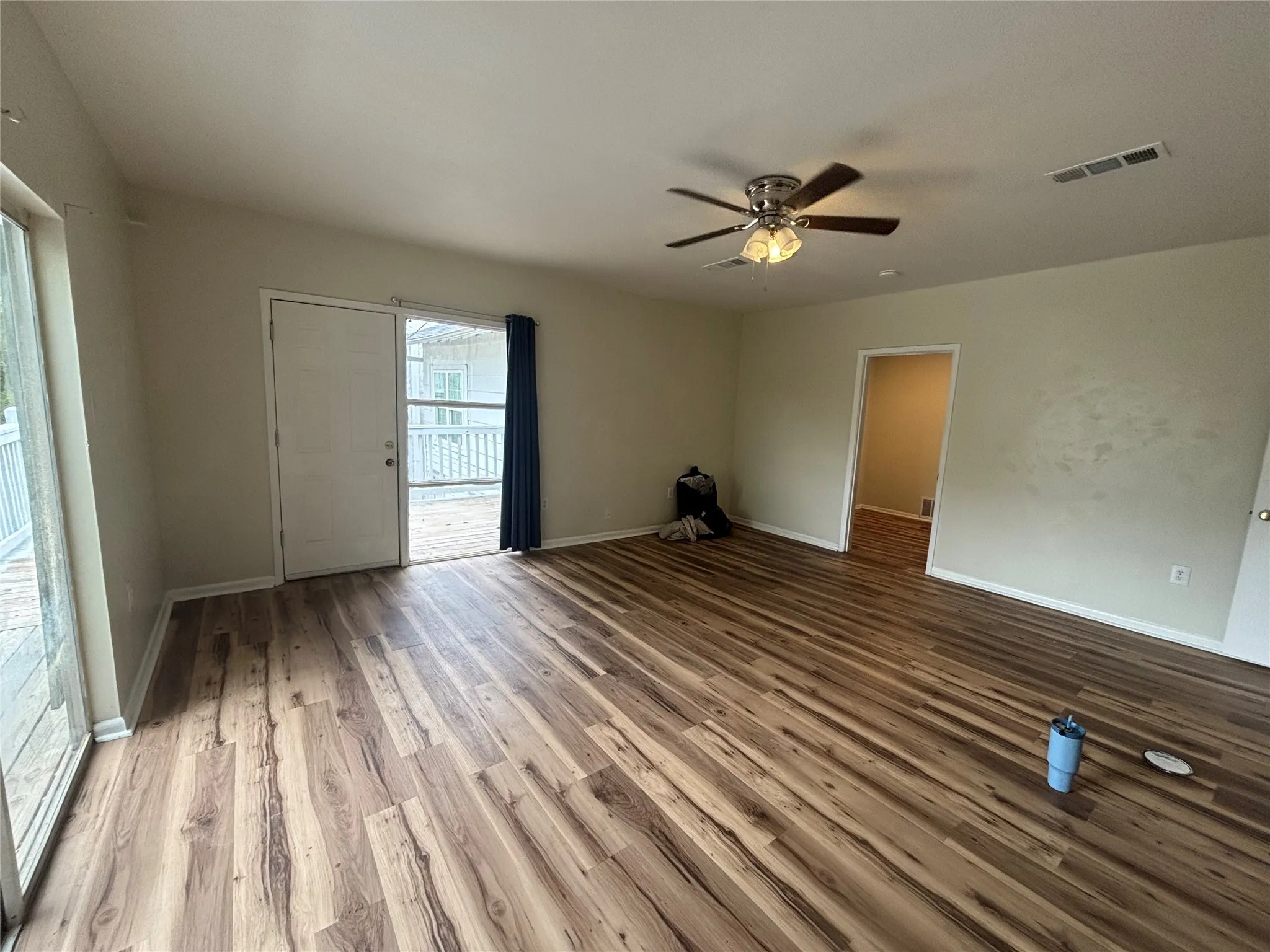 Wood-finish flooring, ceiling fan with light fixture, and sliding glass door to outdoor deck