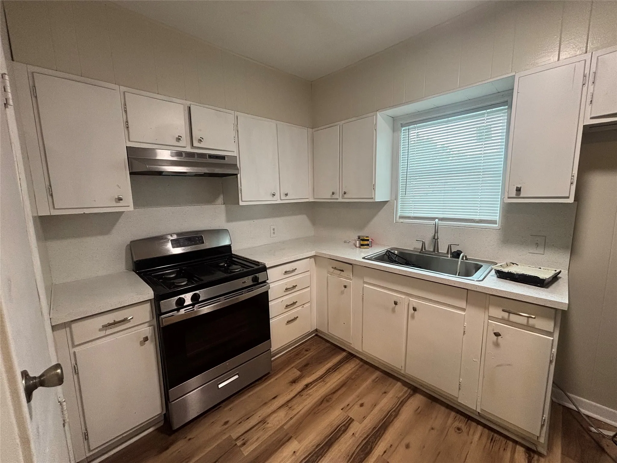 Wood-finish flooring, white cabinetry, stainless steel range, and a window with blinds