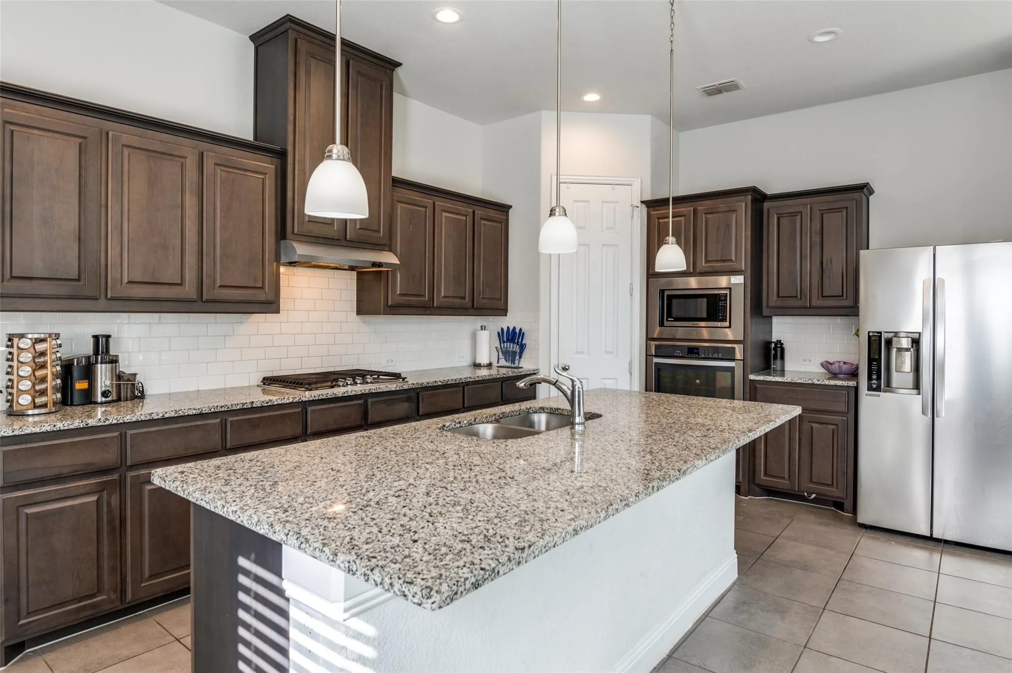 Kitchen featuring a large island with sink, dark wood-finish cabinetry, a subway tile backsplash, and stainless steel appliances