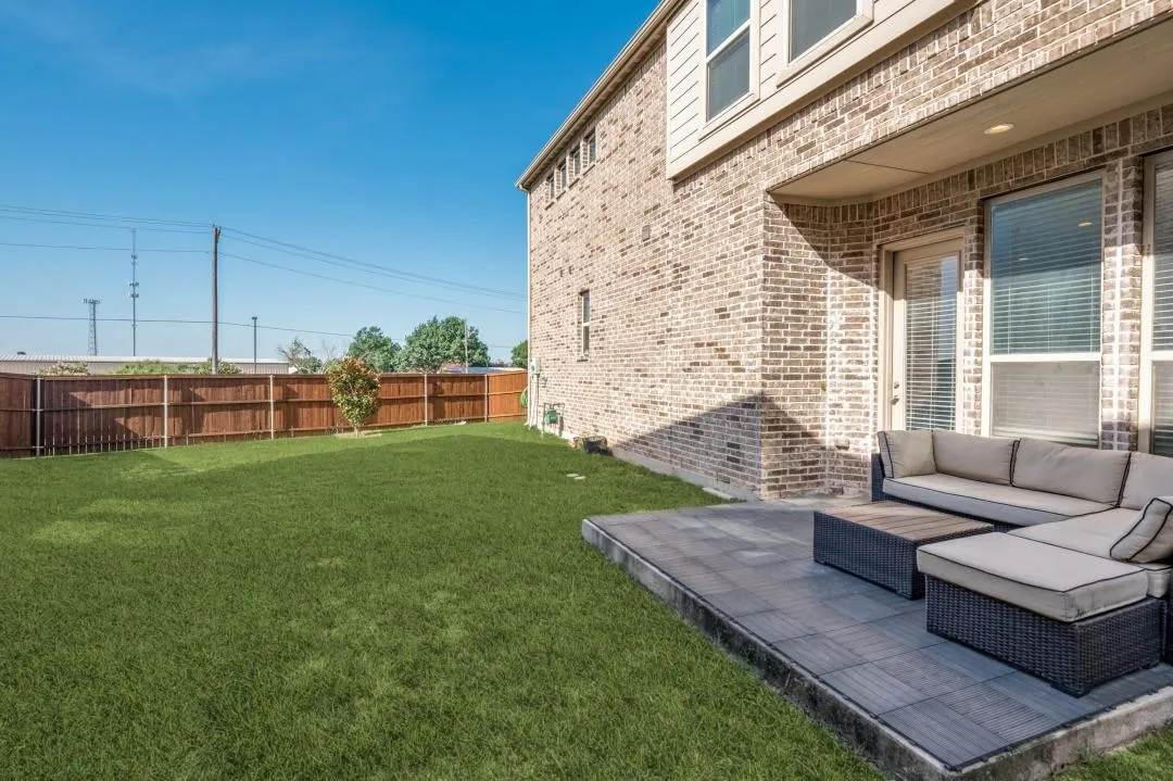 Expansive green lawn, wood fence perimeter, brick exterior, covered patio, and glass-paneled door