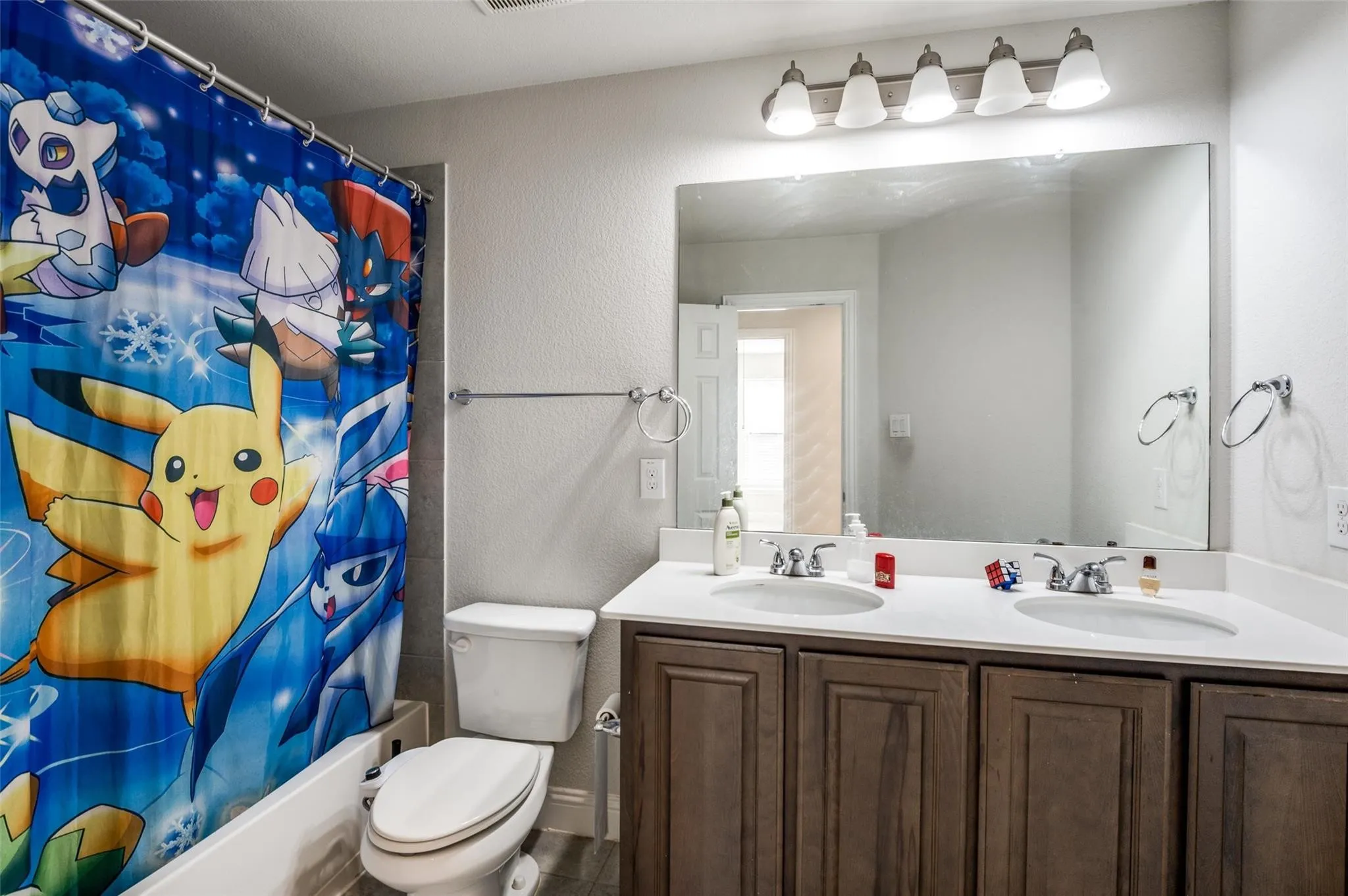 Dual vanity with integrated sinks, white countertops, wood-finish cabinetry, and an expansive wall-mounted mirror