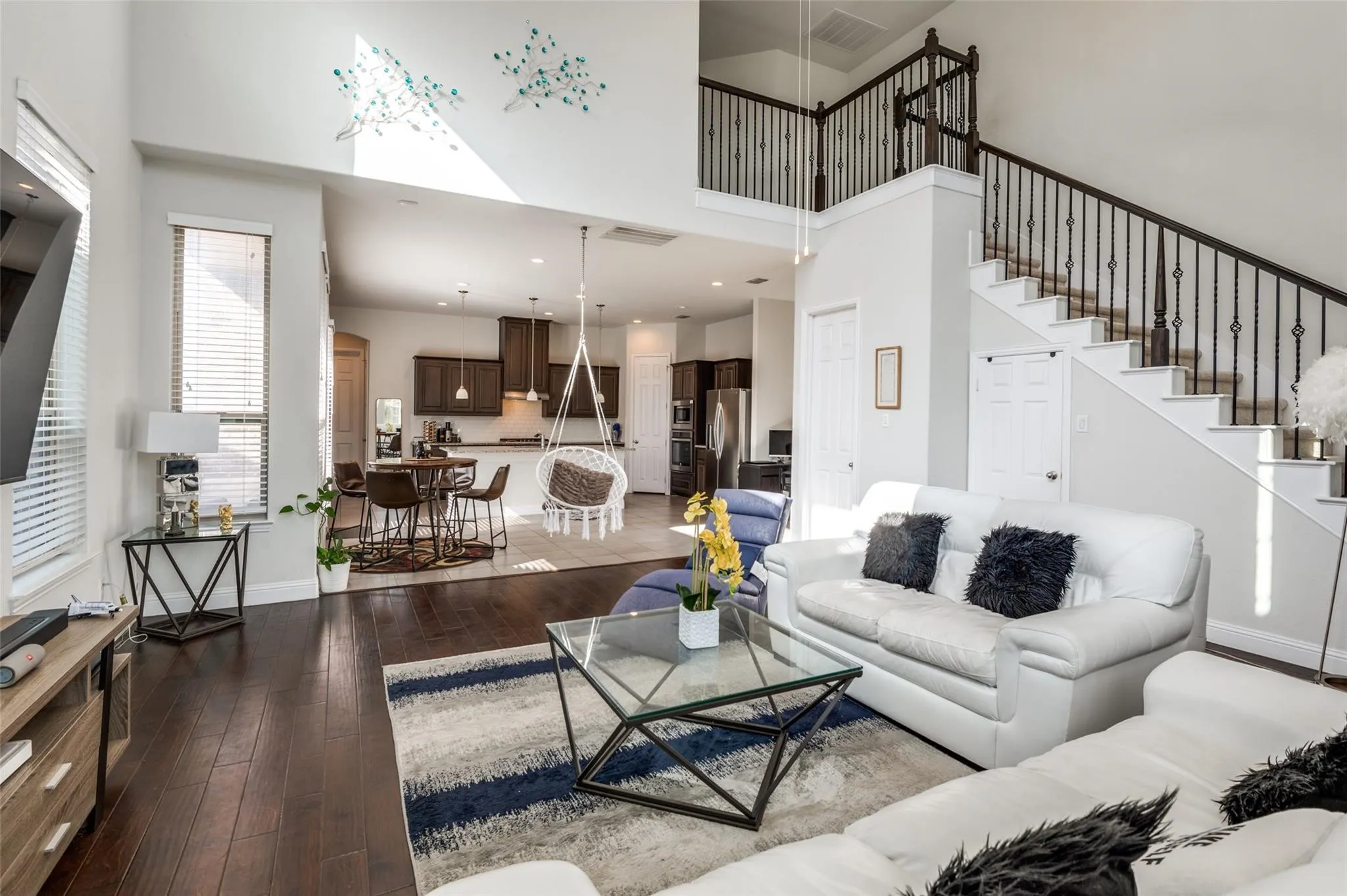 Open-concept living space with dark wood-finish flooring, two-story ceiling, and a prominent staircase featuring decorative iron balusters